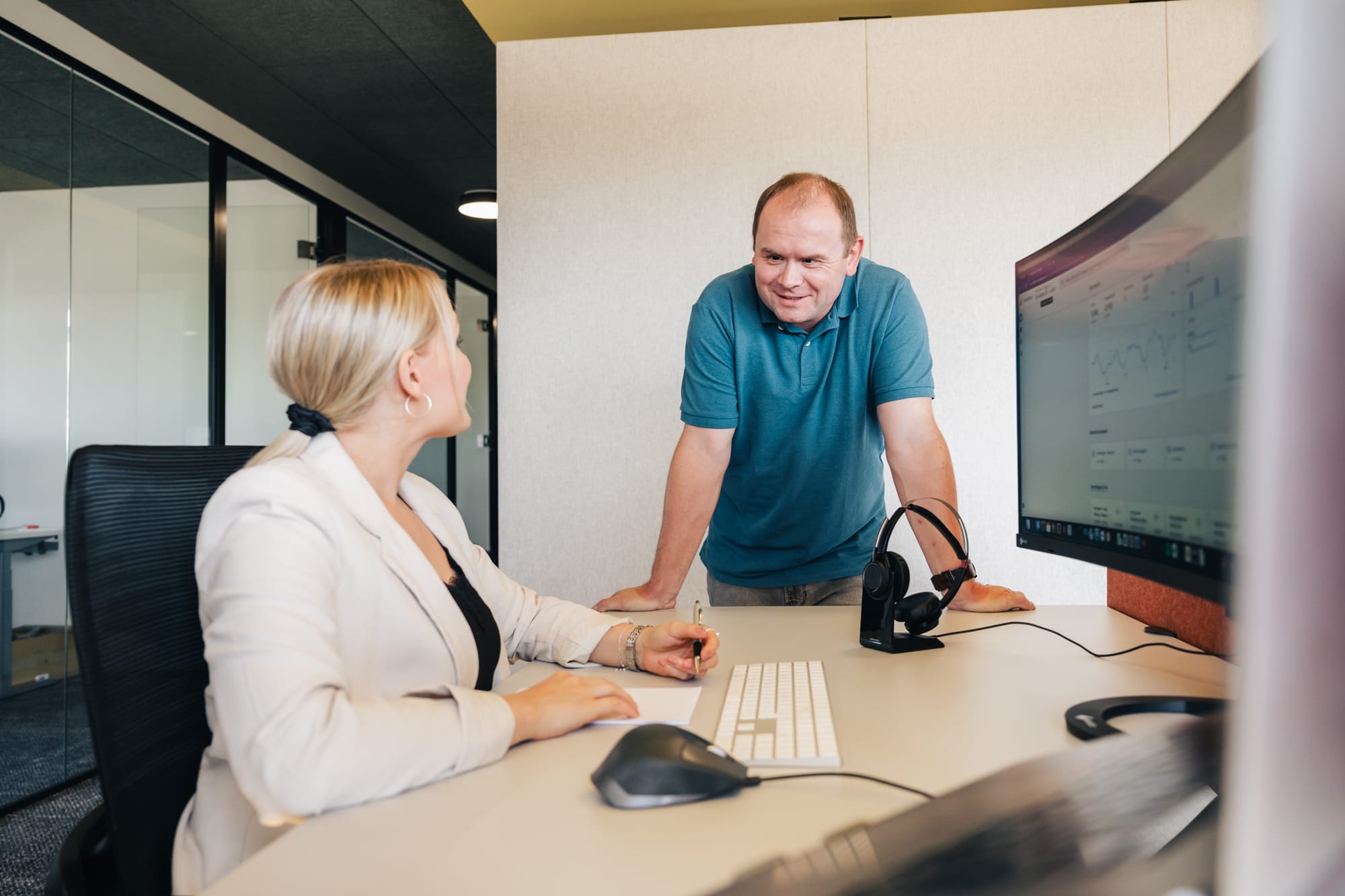 instride Mitarbeiter Troxi steht am Arbeitsplatz von Arbeitskollegin. Gemeinsam besprechen sie Google Analytics.