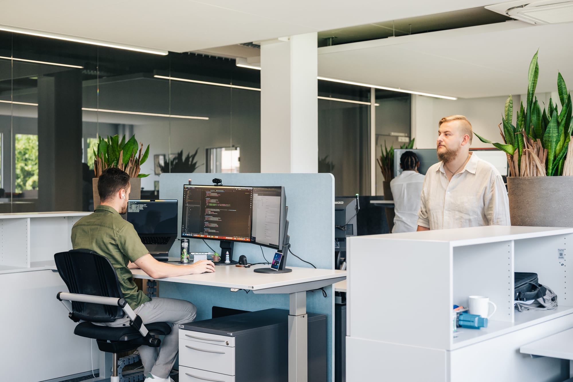 instride Bürosituation: 2 Entwickler codieren am Arbeitsplatz, 3. Entwickler läuft durch den Gang