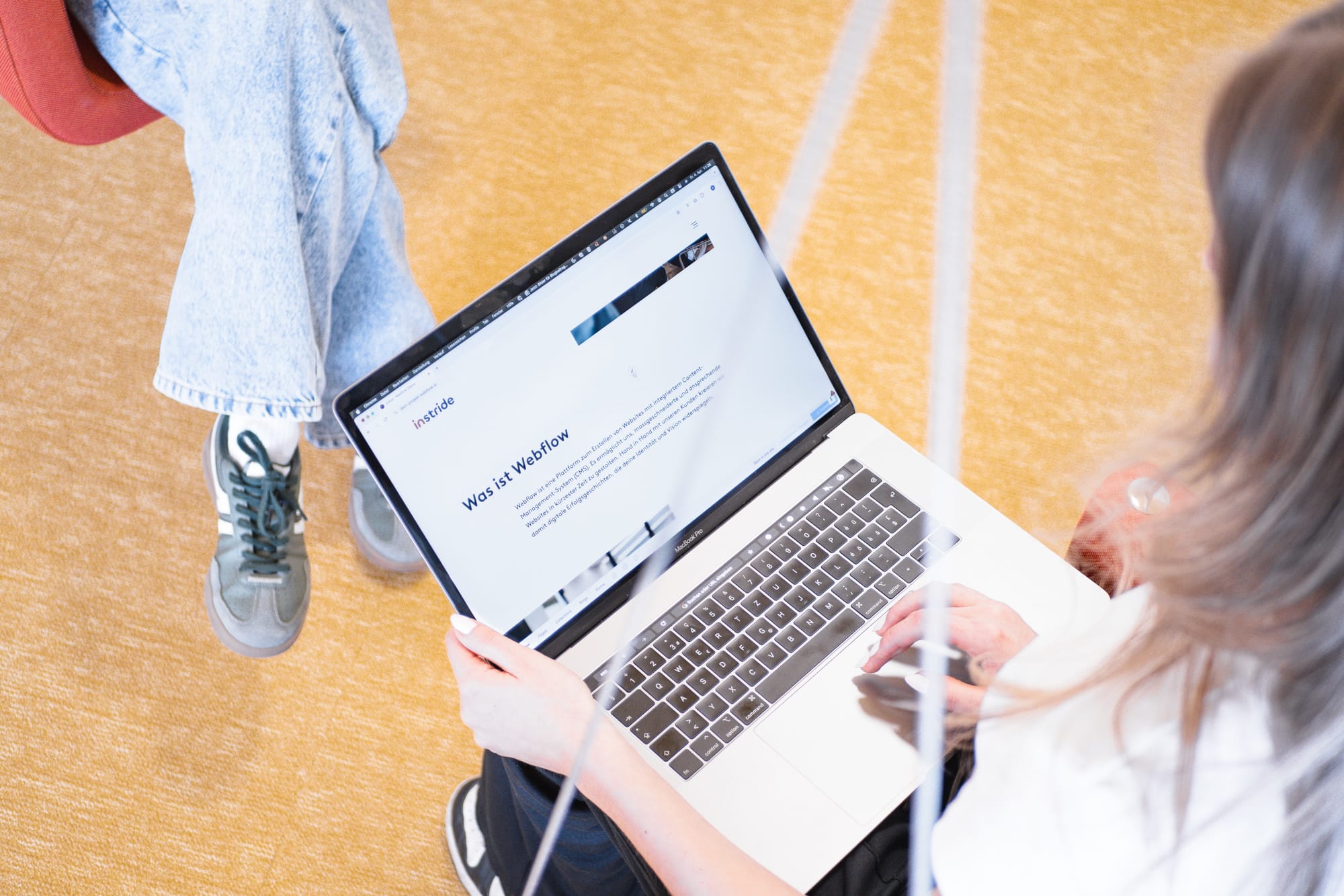 Zwei Personen im kreativen Austausch – eine Person arbeitet am Laptop mit geöffneter Webflow-Seite der Digitalagentur instride AG, während die andere entspannt gegenüber sitzt.
