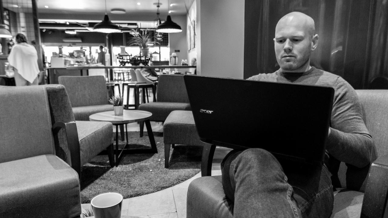 Fotografi av mann som sitter på kafe med datamaskin i fanget