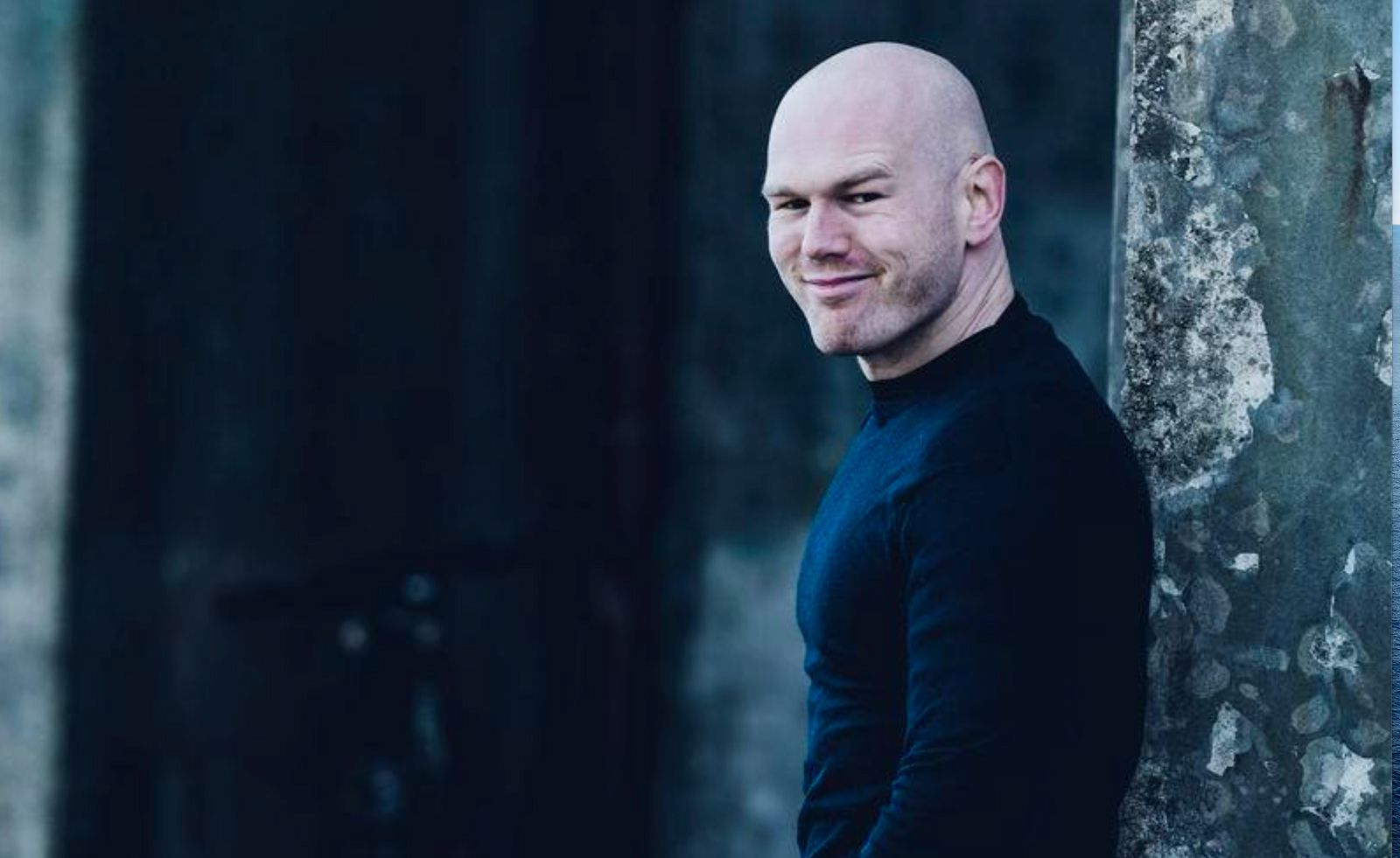 Fotografi av en mann som står med ryggen mot et tre og smiler.