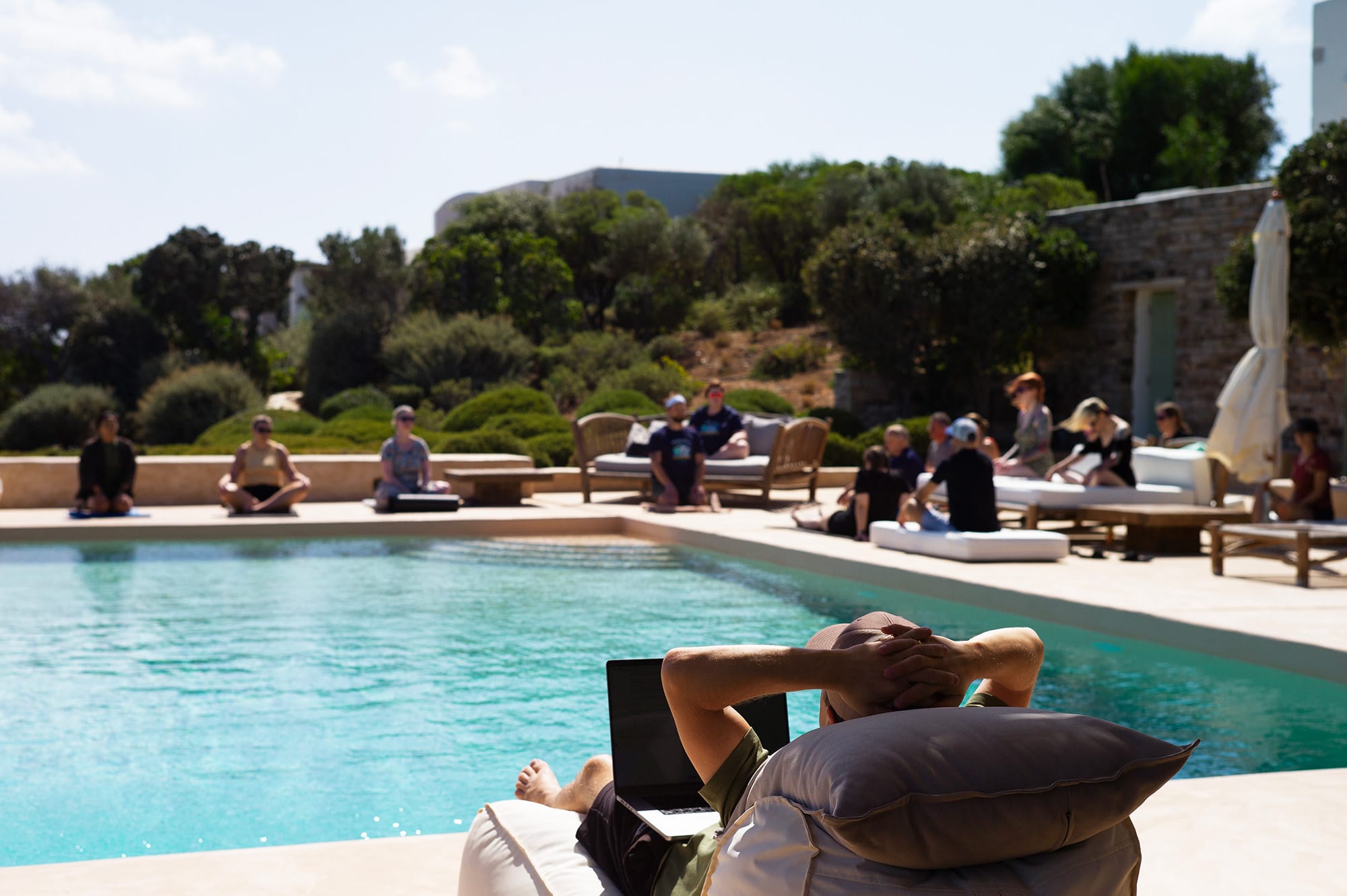Fotografi av en person som sitter på solseng ved en bassengkant.