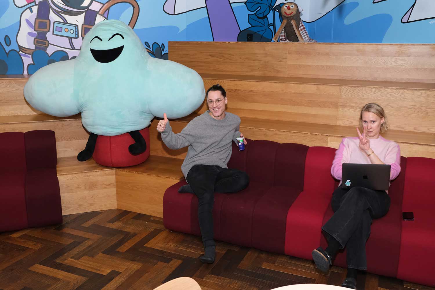 Fotografi av to ansatte på marked i Fiken som sitter i en sofa ved siden av Fikens maskott