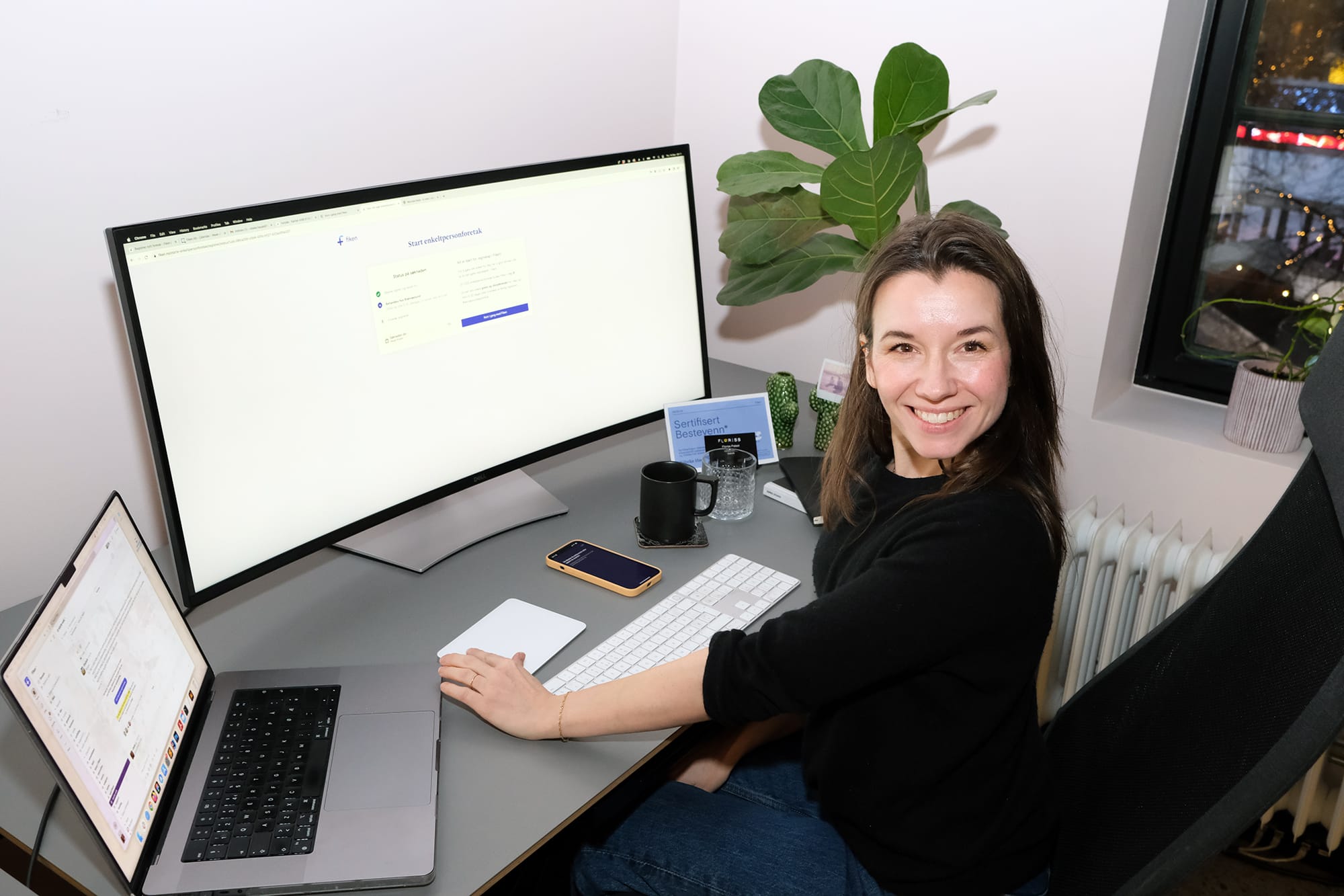 Fotografi av Vibeke foran PC-en sin, smilende.
