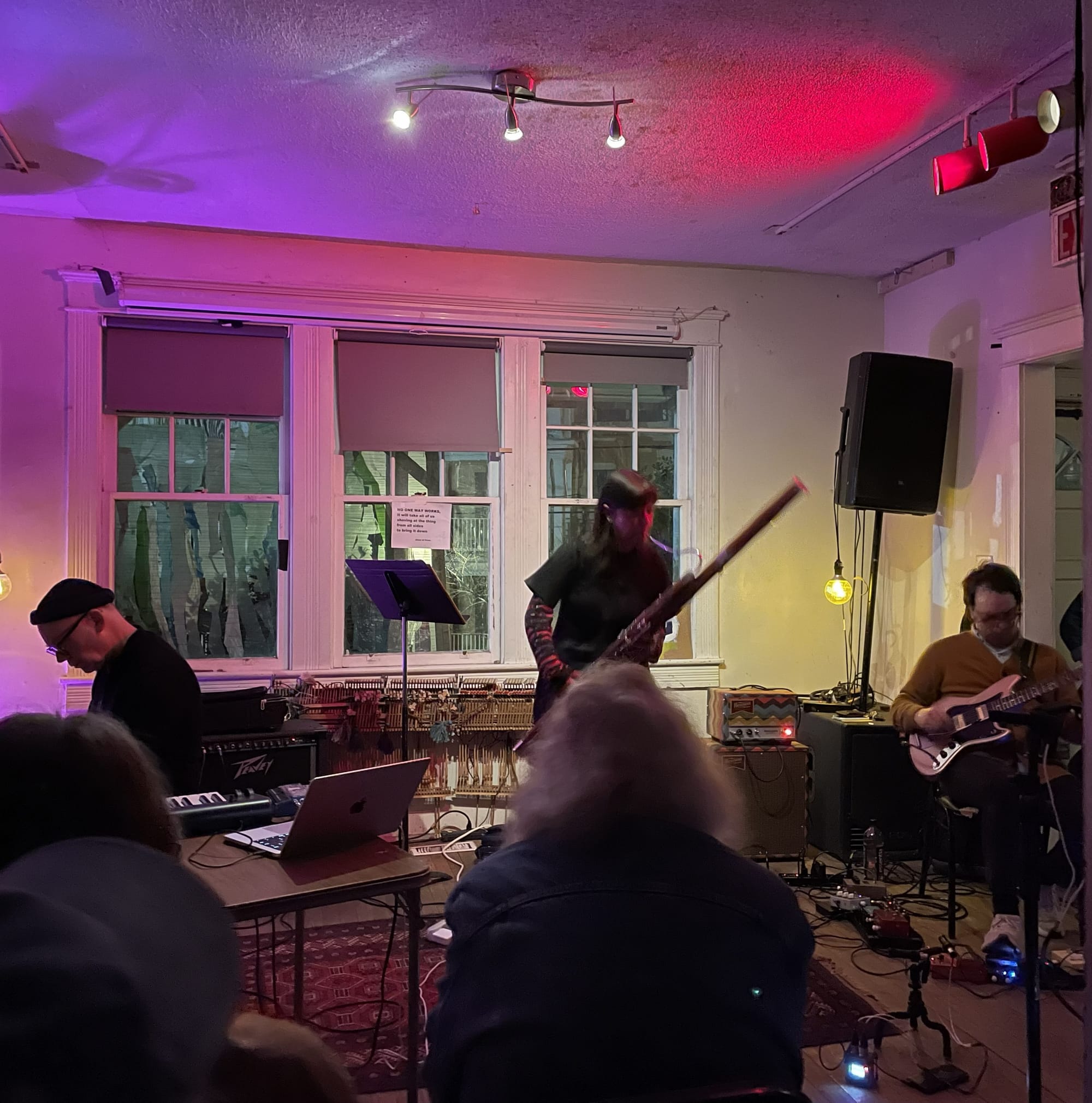 A pianist, bassoonist, and guitarist perform in front of a small crowd in a living room.