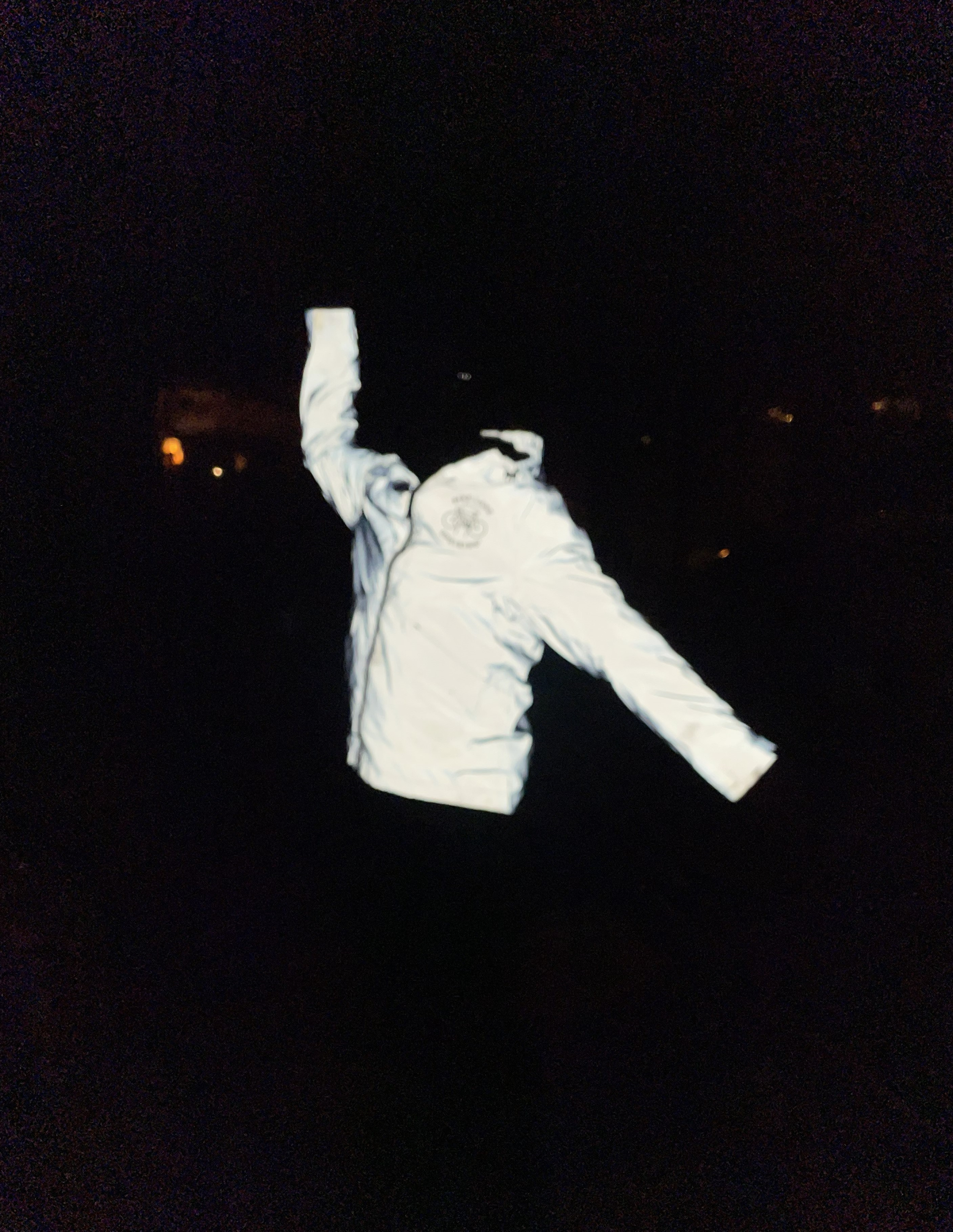 A brightly reflective white coat in an action pose on a black background, obscuring who is wearing it.