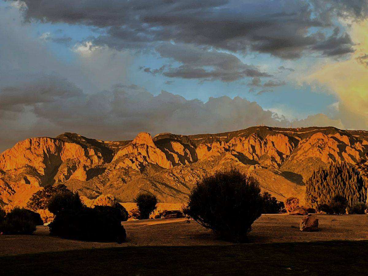 Mountains glow orange and pink behind a darkened foreground. A moody sky of of blue, purple,and pink dominates the top part of the photo.