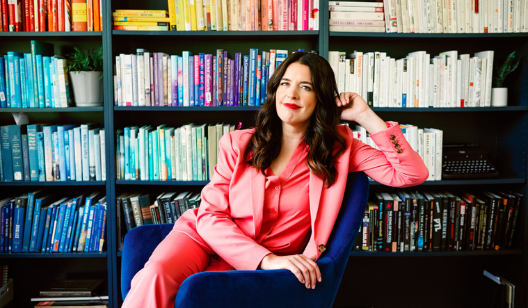 Kate Bowler sits in front of a colorful bookshelf.