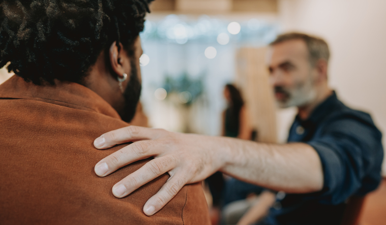 A man puts his hand on a friend's shoulder offering support.