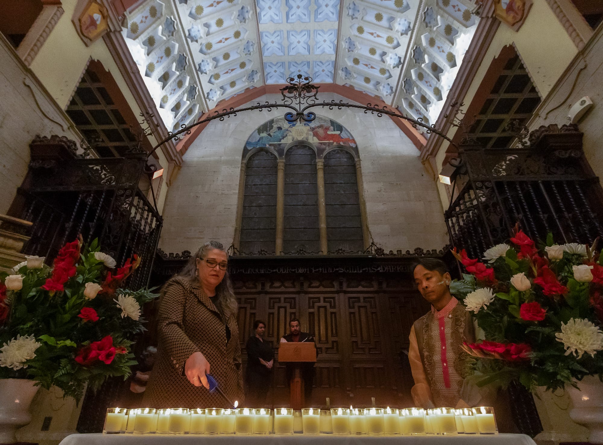 Two people light numerous candles inside a chapel.
