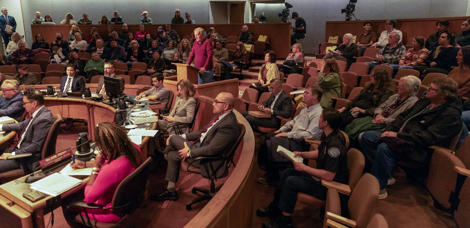 Dozens of people site in a city council chamber.