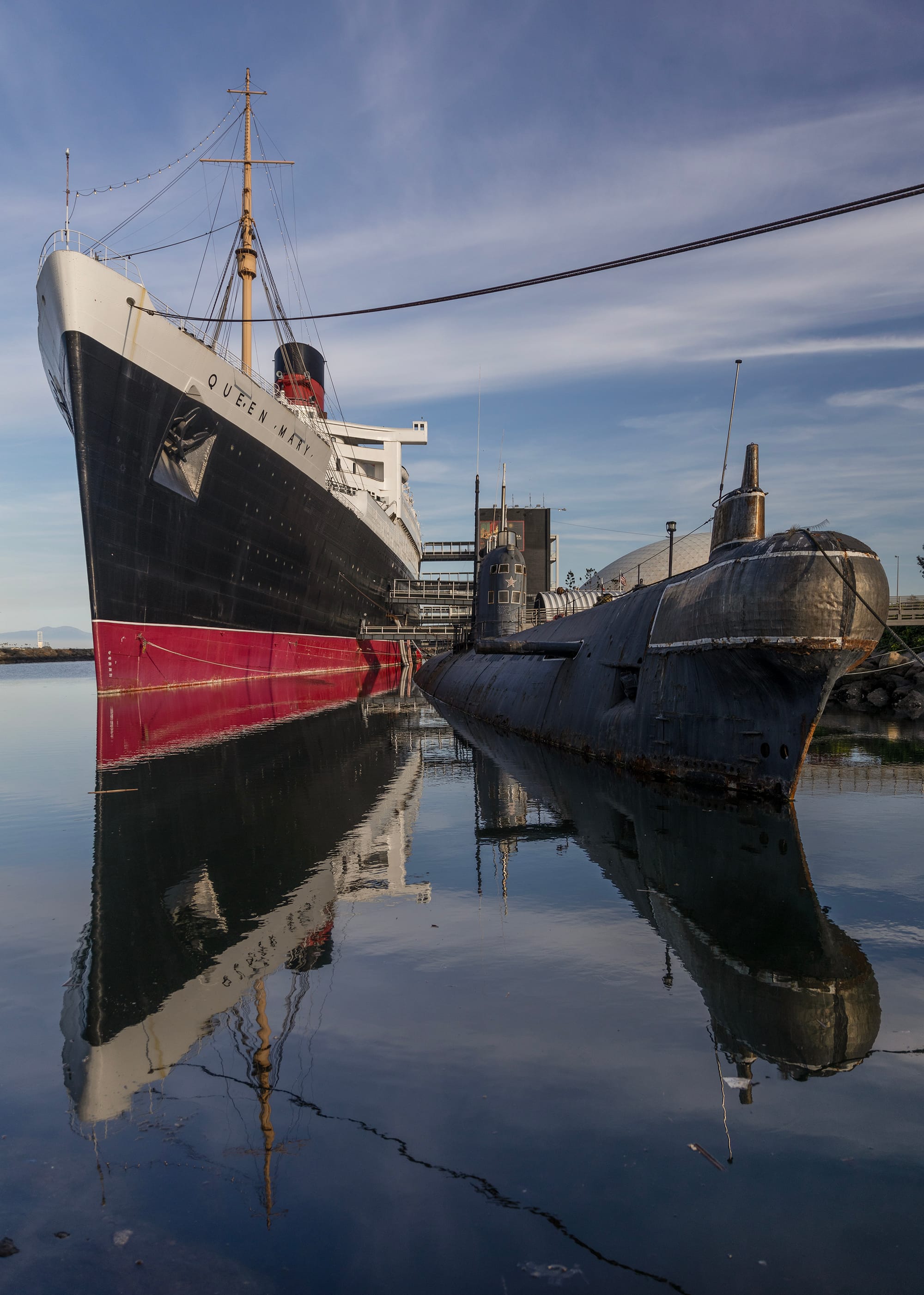 A rusting submarine sits beside a historic red, black and white ocean liner.