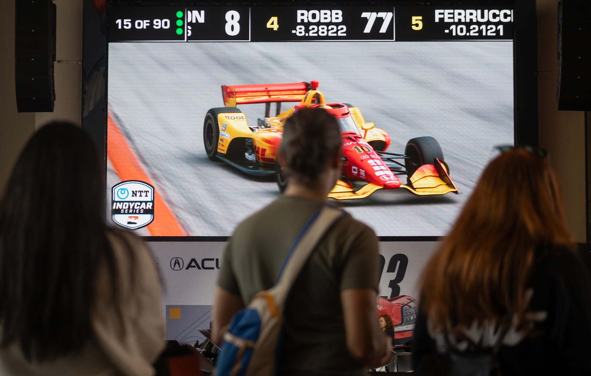 People stare at a tv screen showing a red and yellow race car.