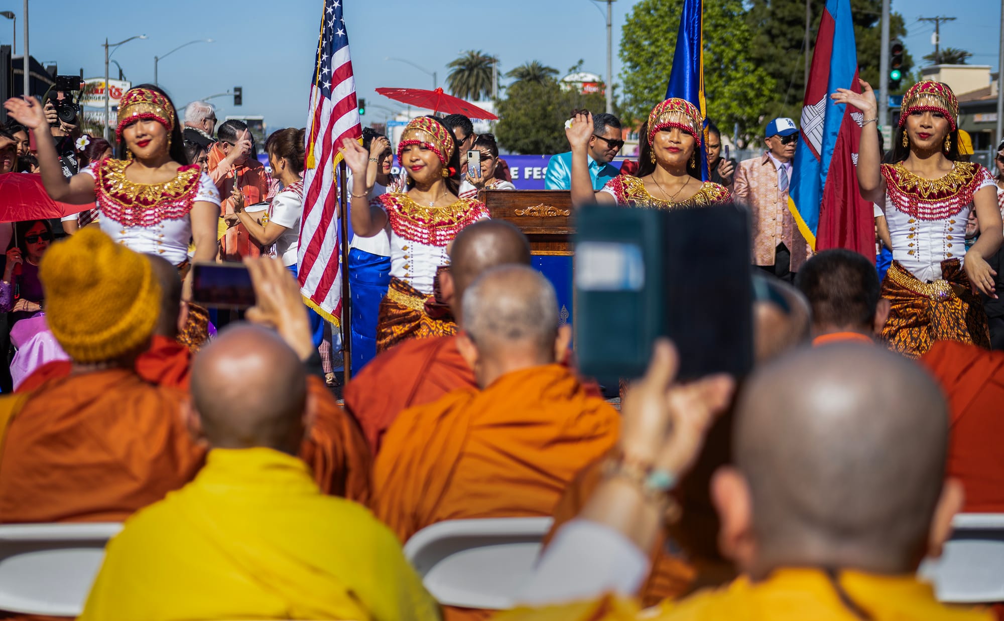 People in orange robes watch dancers outside.