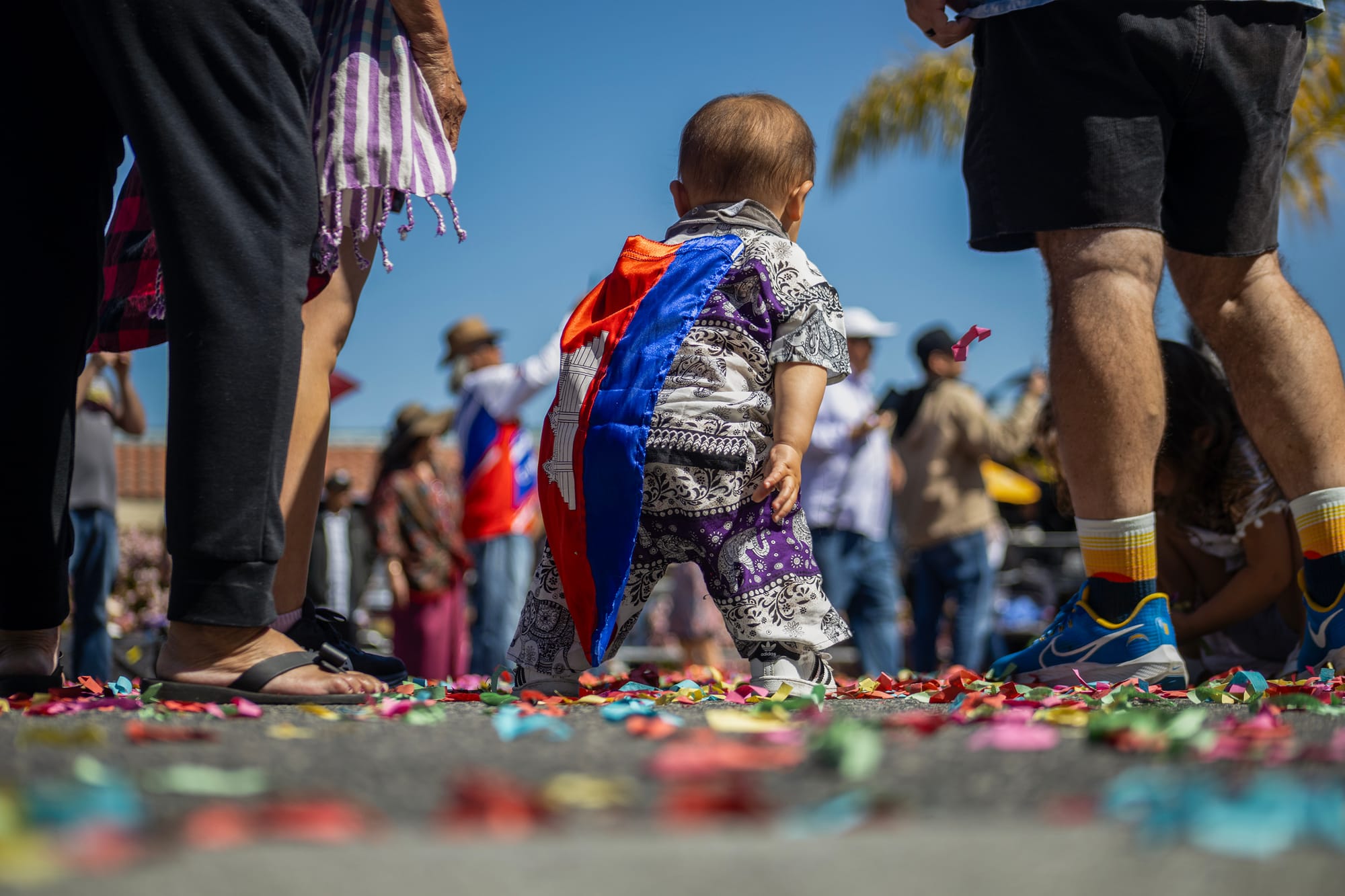 A toddler stands in the street with a crowd of people nearby.