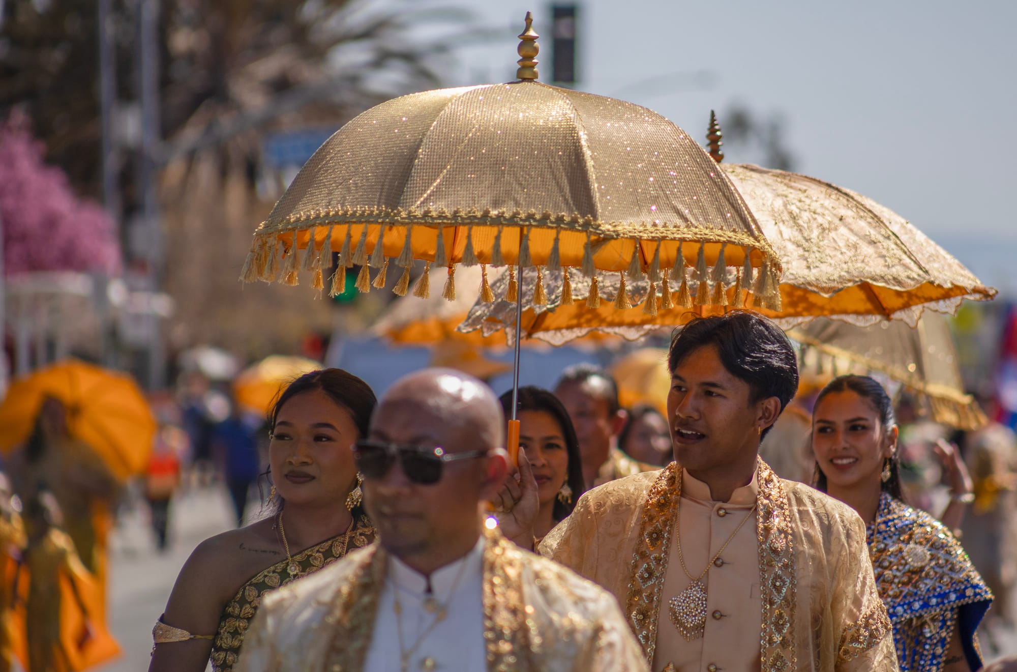 A group of people walk while holding gold umbrellas above them.