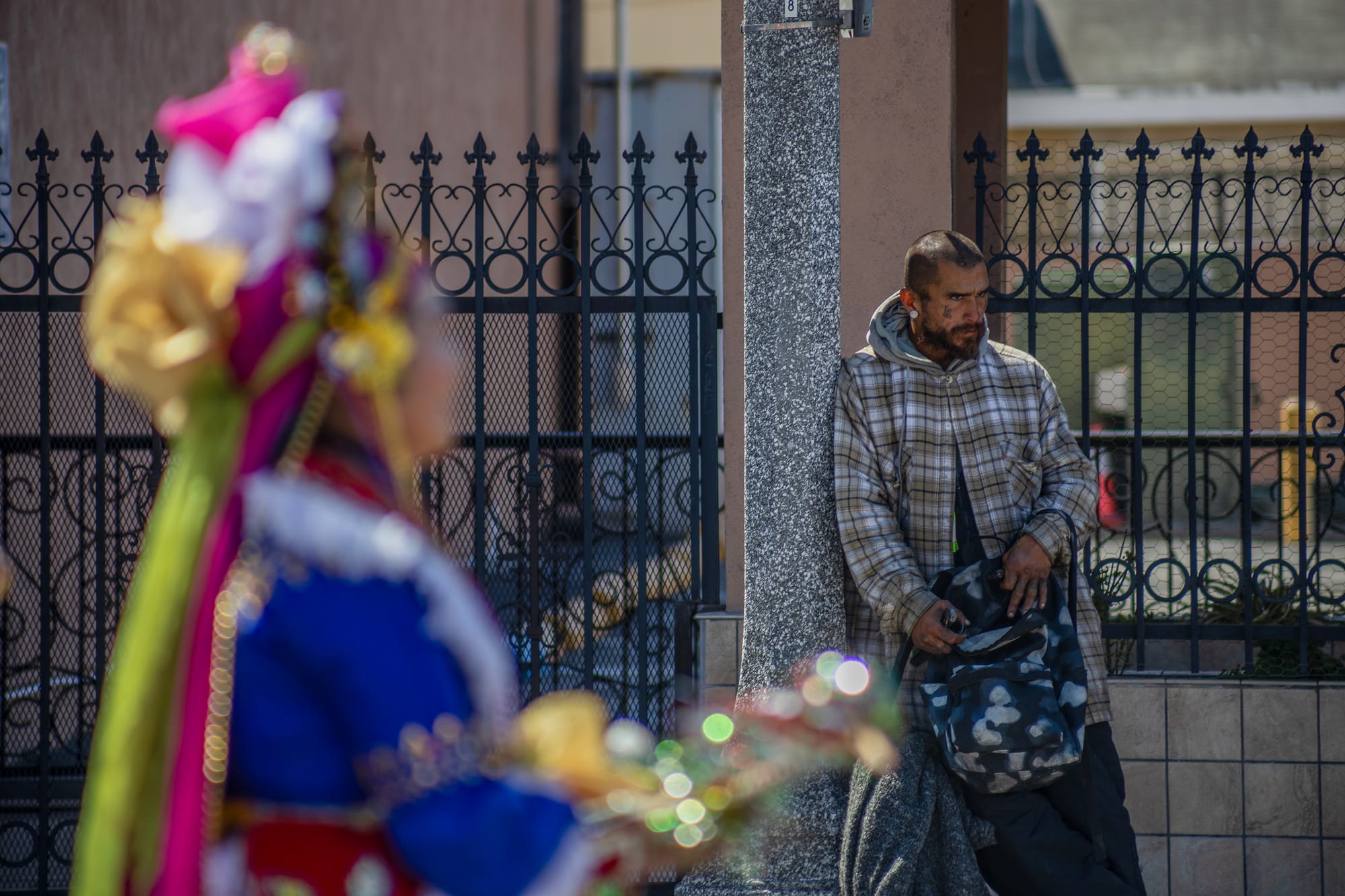 A man leans against a light post as a person wearing brightly colored robes walks by.