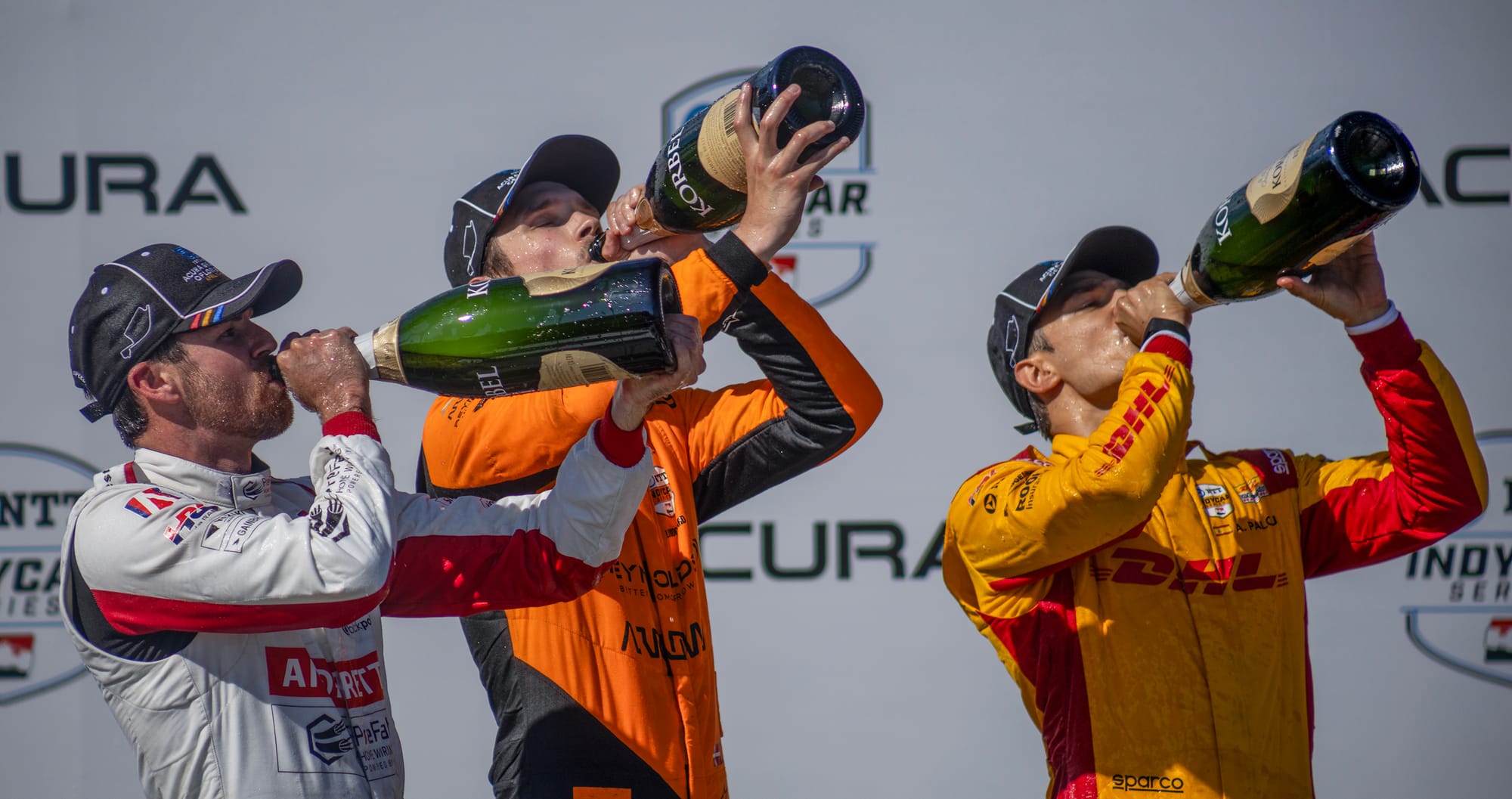 Three men drink champagne straight from the bottle.