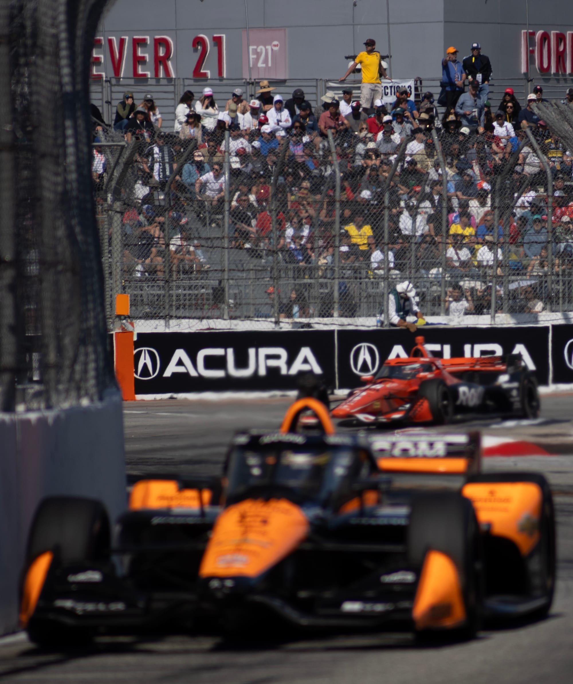 Two race cars speed past bleachers full of people.