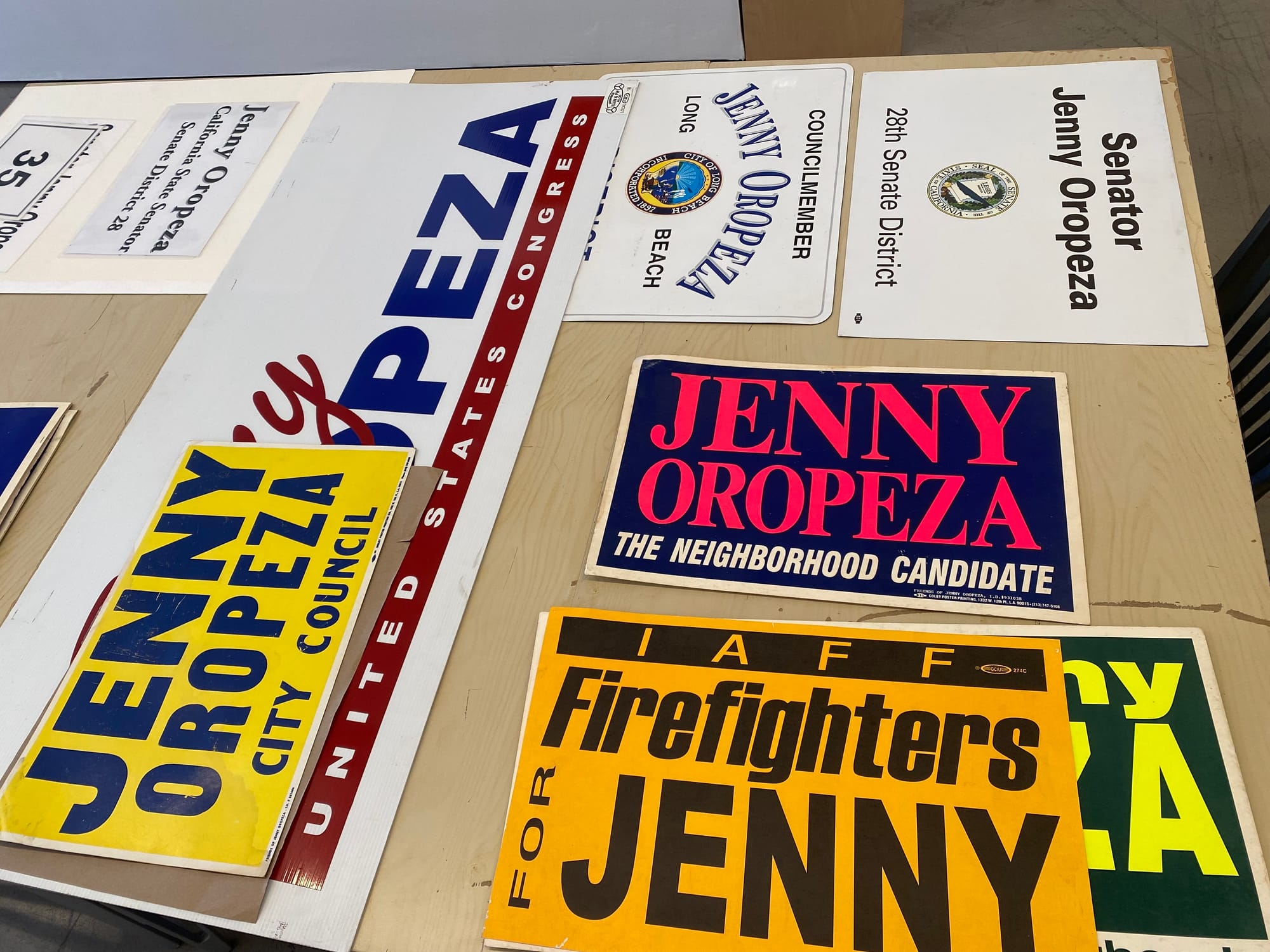 Assorted Jenny Oropeza campaign signs lying on a table.