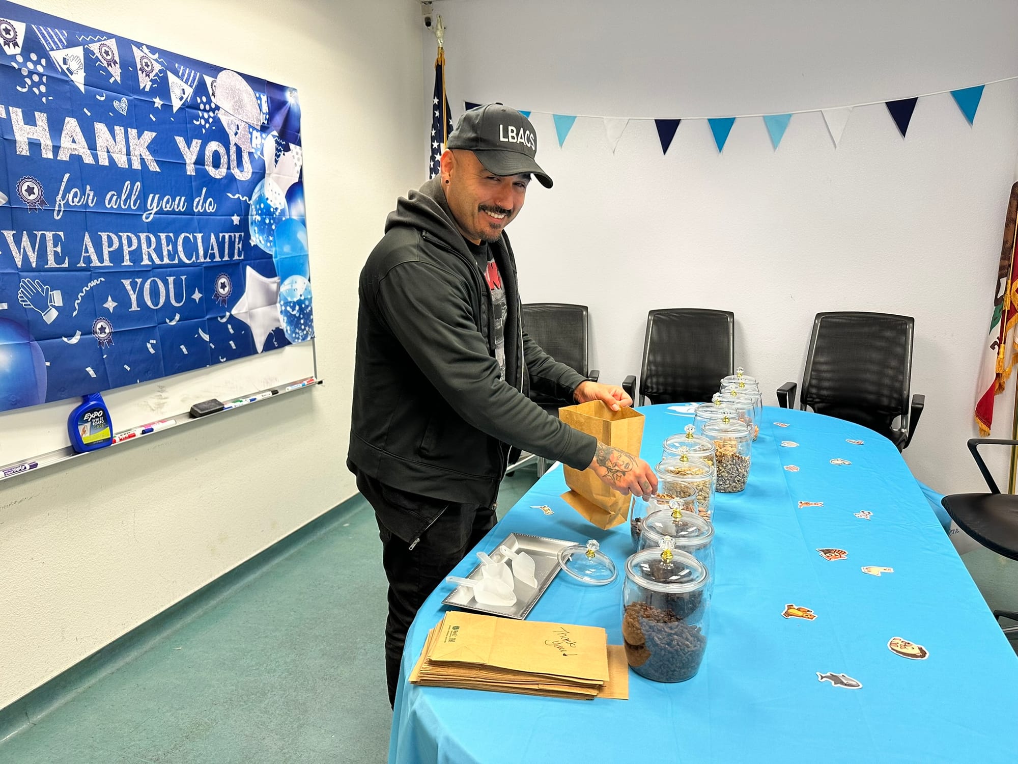 A man smiles while standing at a blue table.
