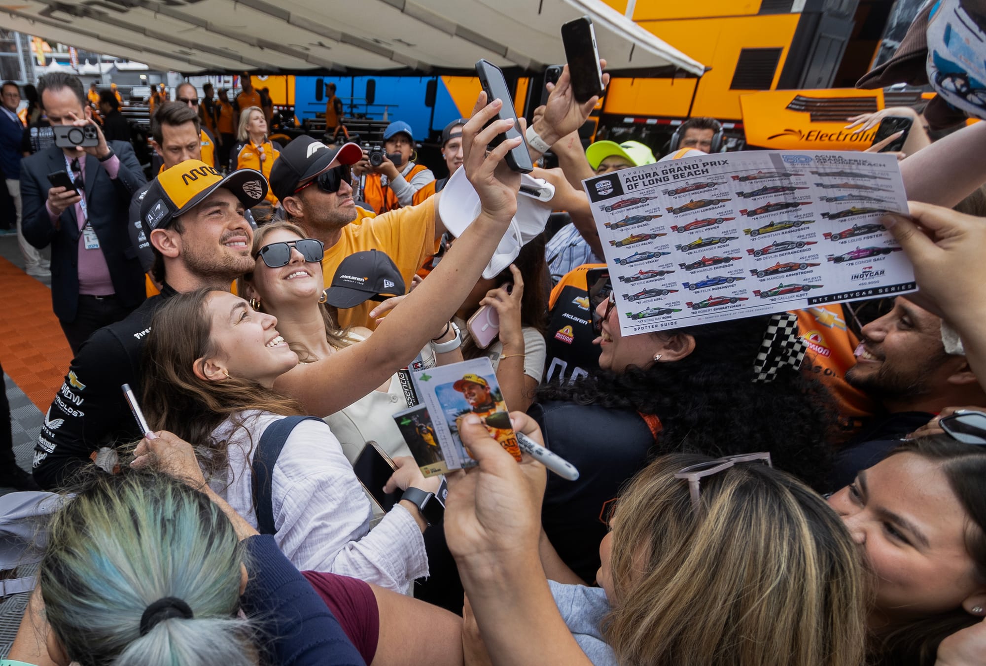 A man takes a phone selfie with people in a crowd.