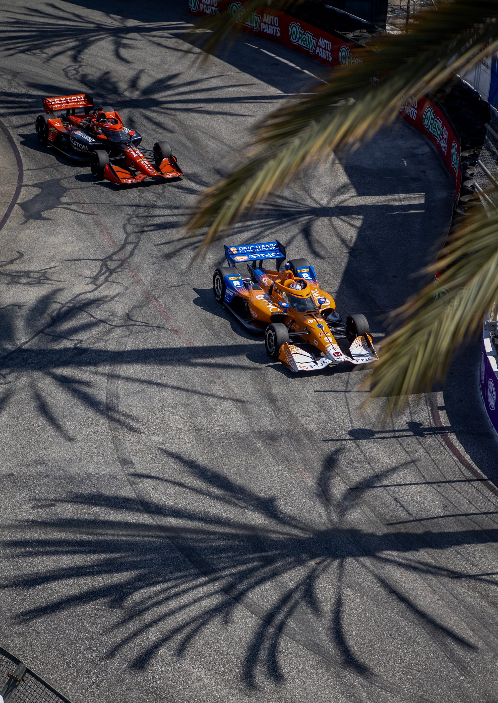 An orange and blue race car leads a black and red race car.