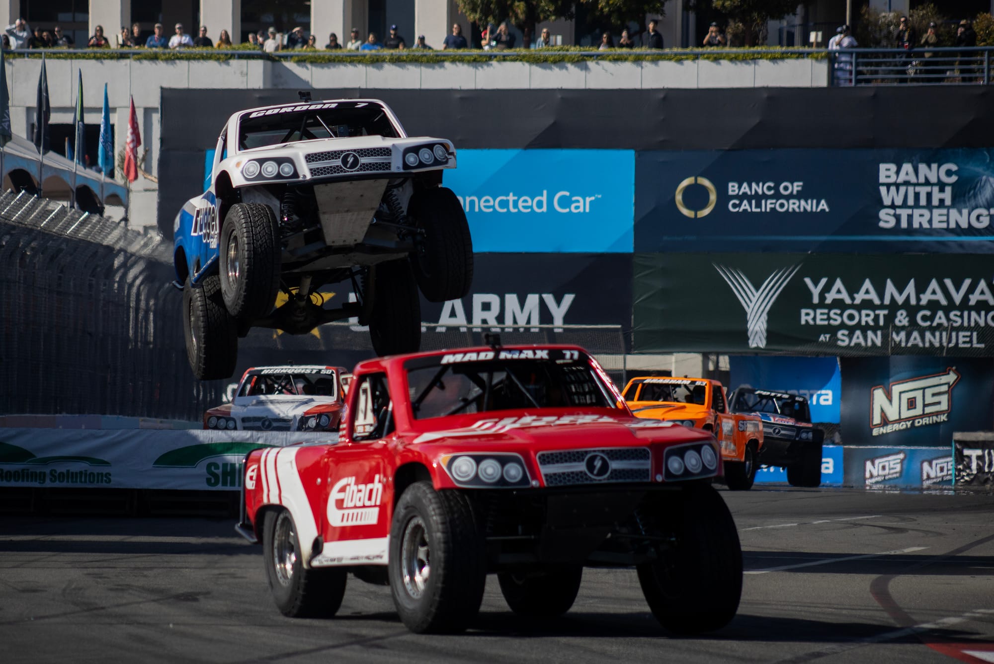 A blue and white truck is flying a few feet off the ground behind a red and white truck.