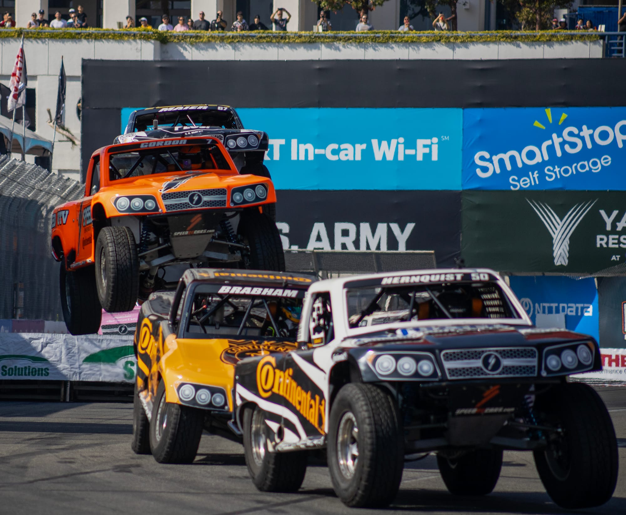Different colored trucks fly off ramps during a race event.