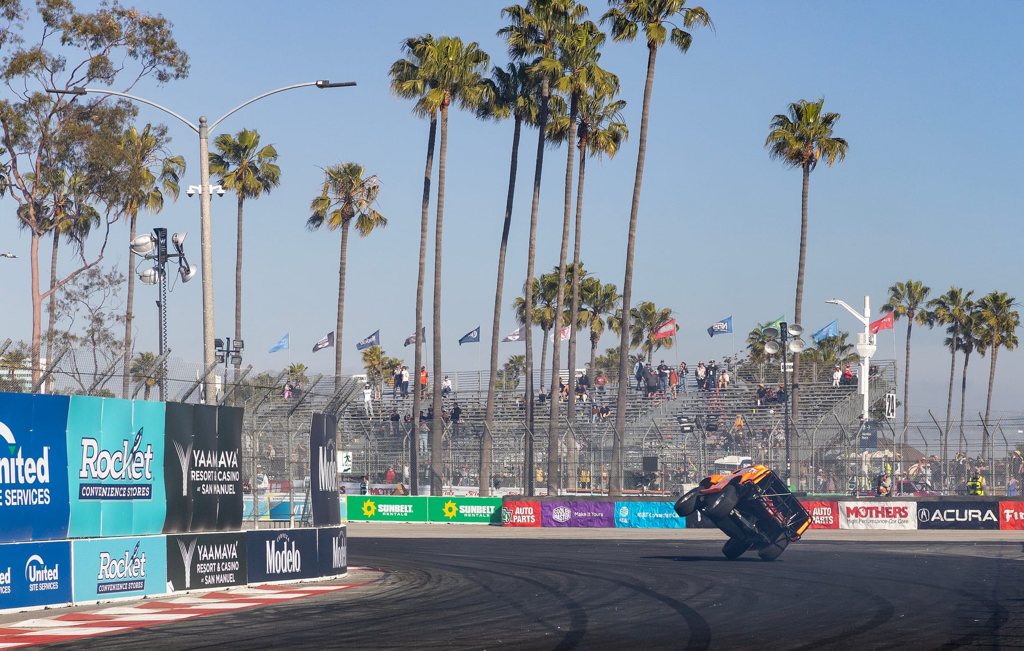 An orange truck is tipped on two wheels as it drives on a race track.
