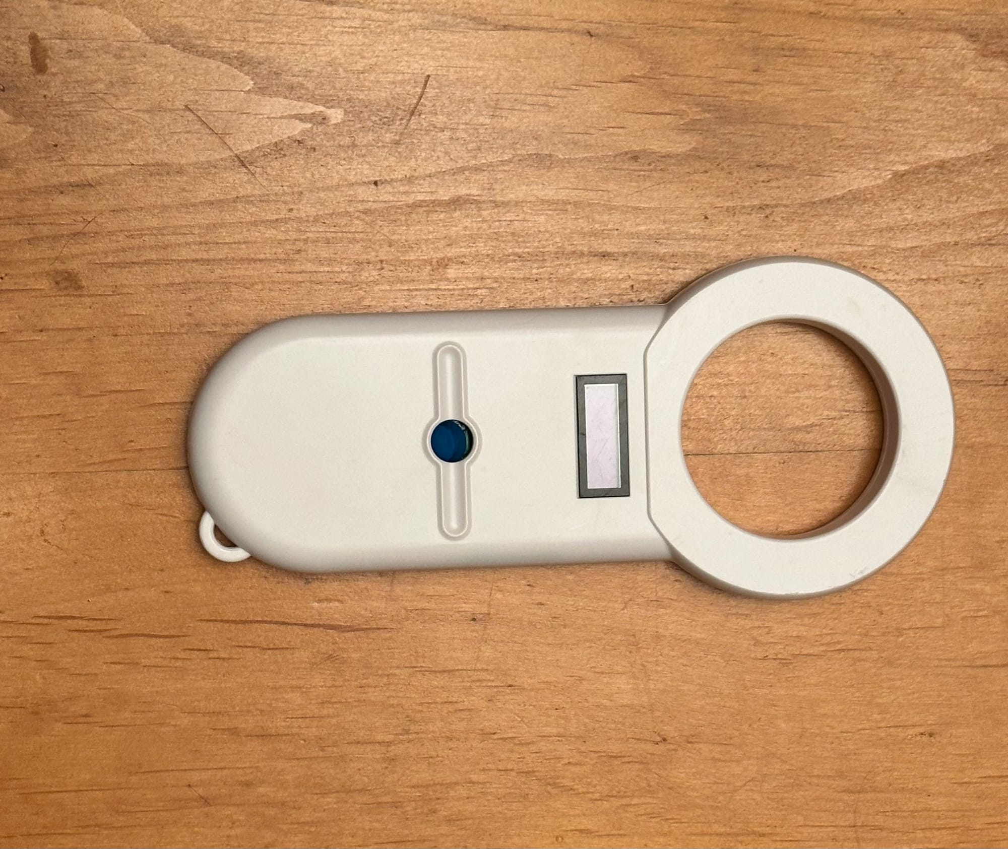 A white plastic device with a large ring at one end resting on a wood table.