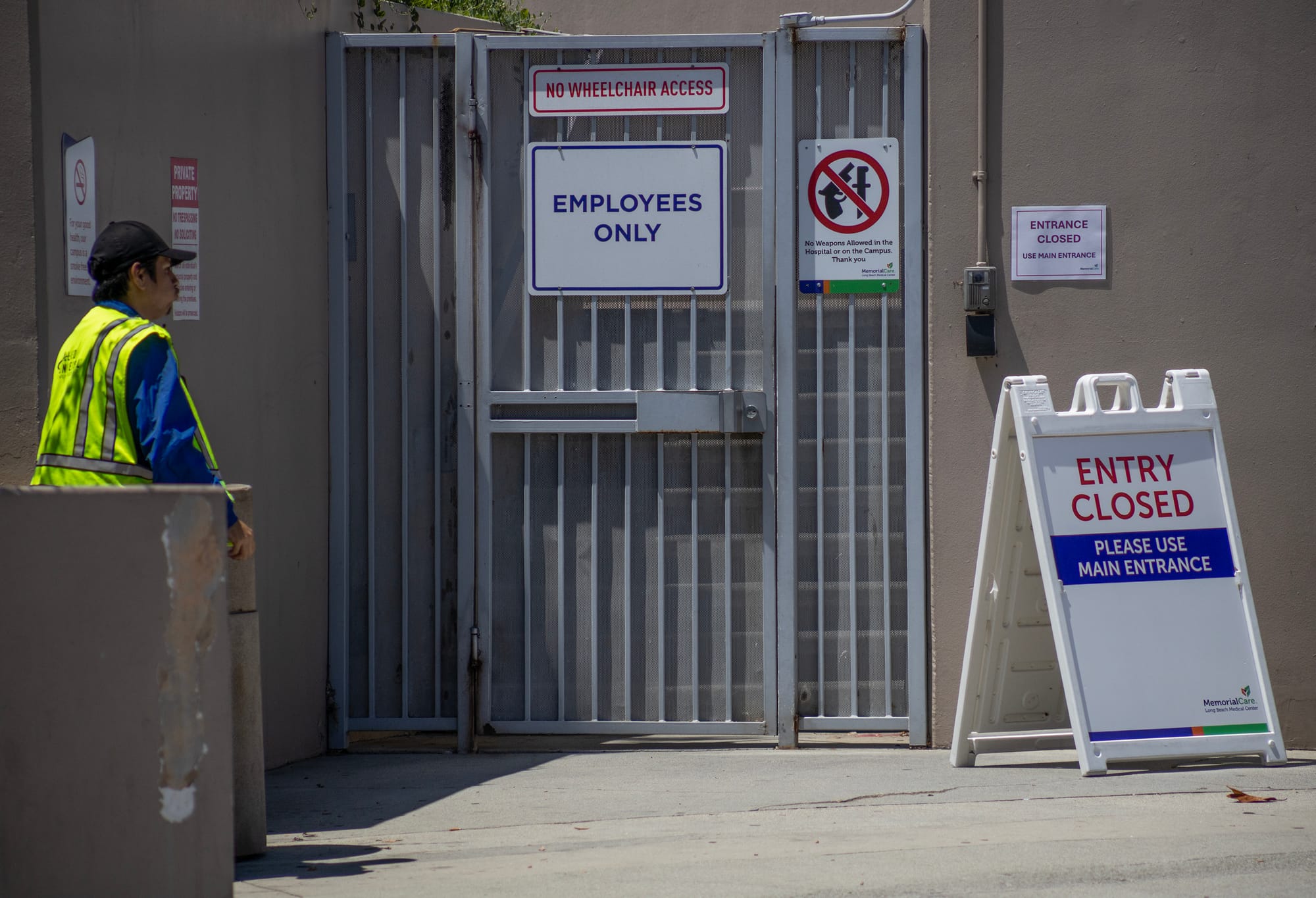 A man in a neon green vest stands next to a gray gate labeled "employees only."