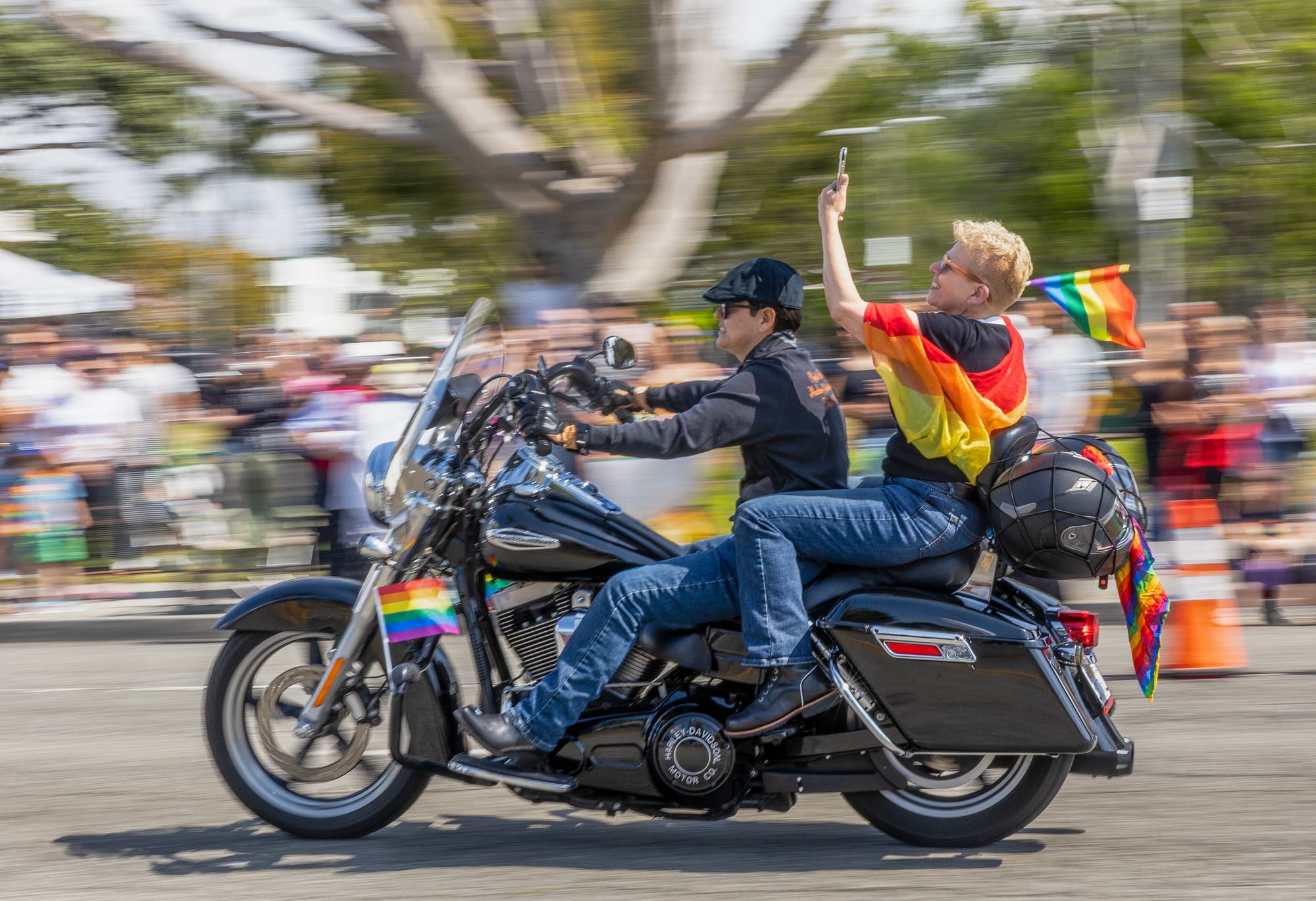 Two people ride a motorcycle in front of a blurry crowd of people.