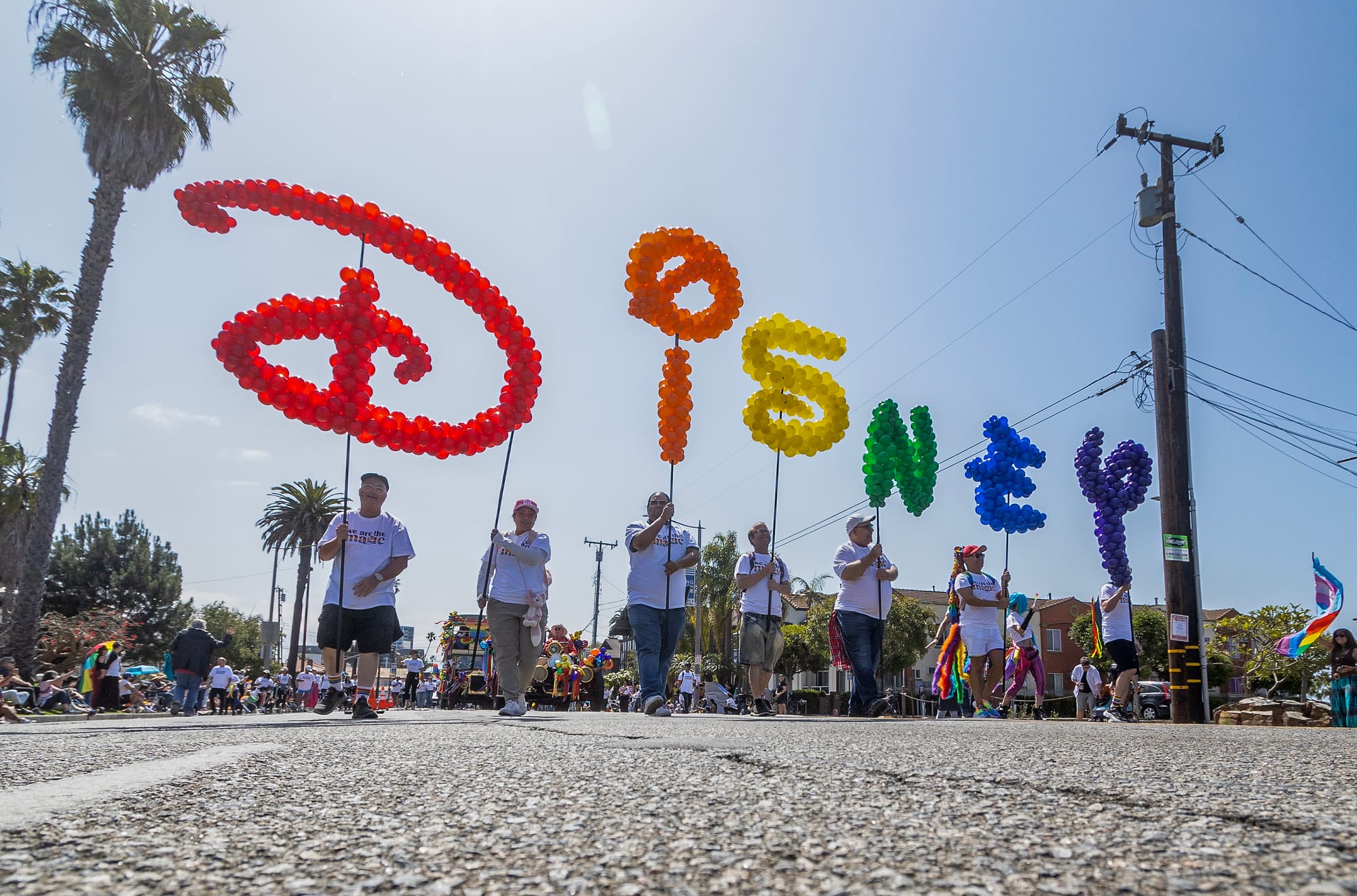 People march on a street carrying rainbow-colored letters that spell out "Disney."