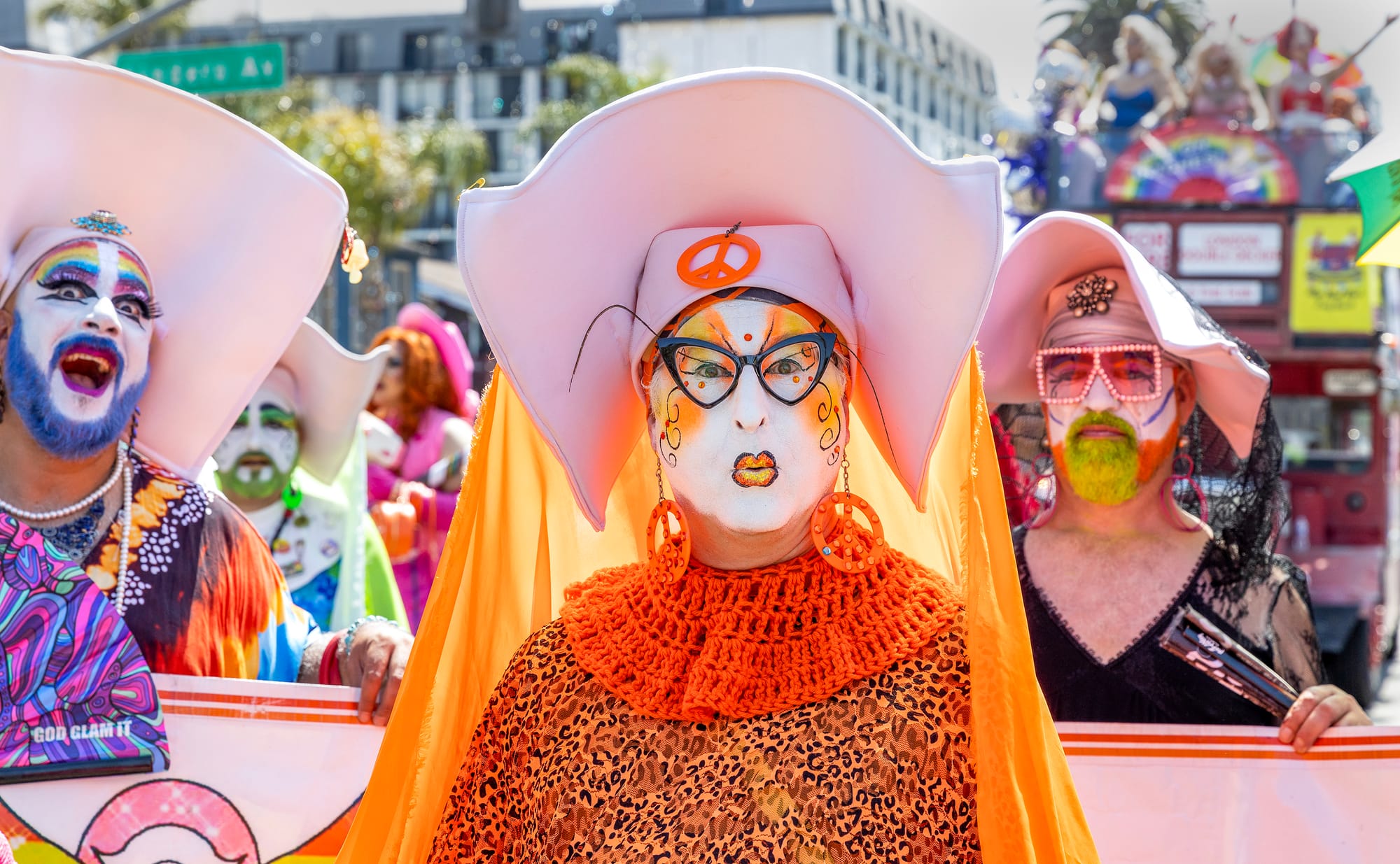 People with elaborate and colorful faceprint and hats stand outside.