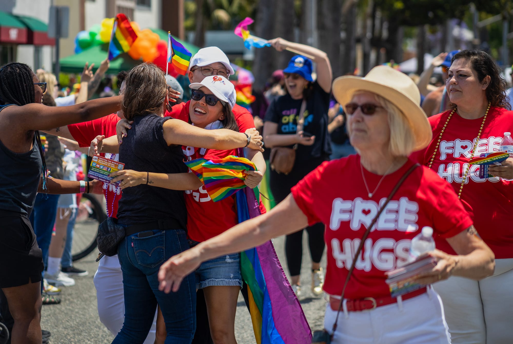 People wearing red shirts that say "free hugs" hug other people.