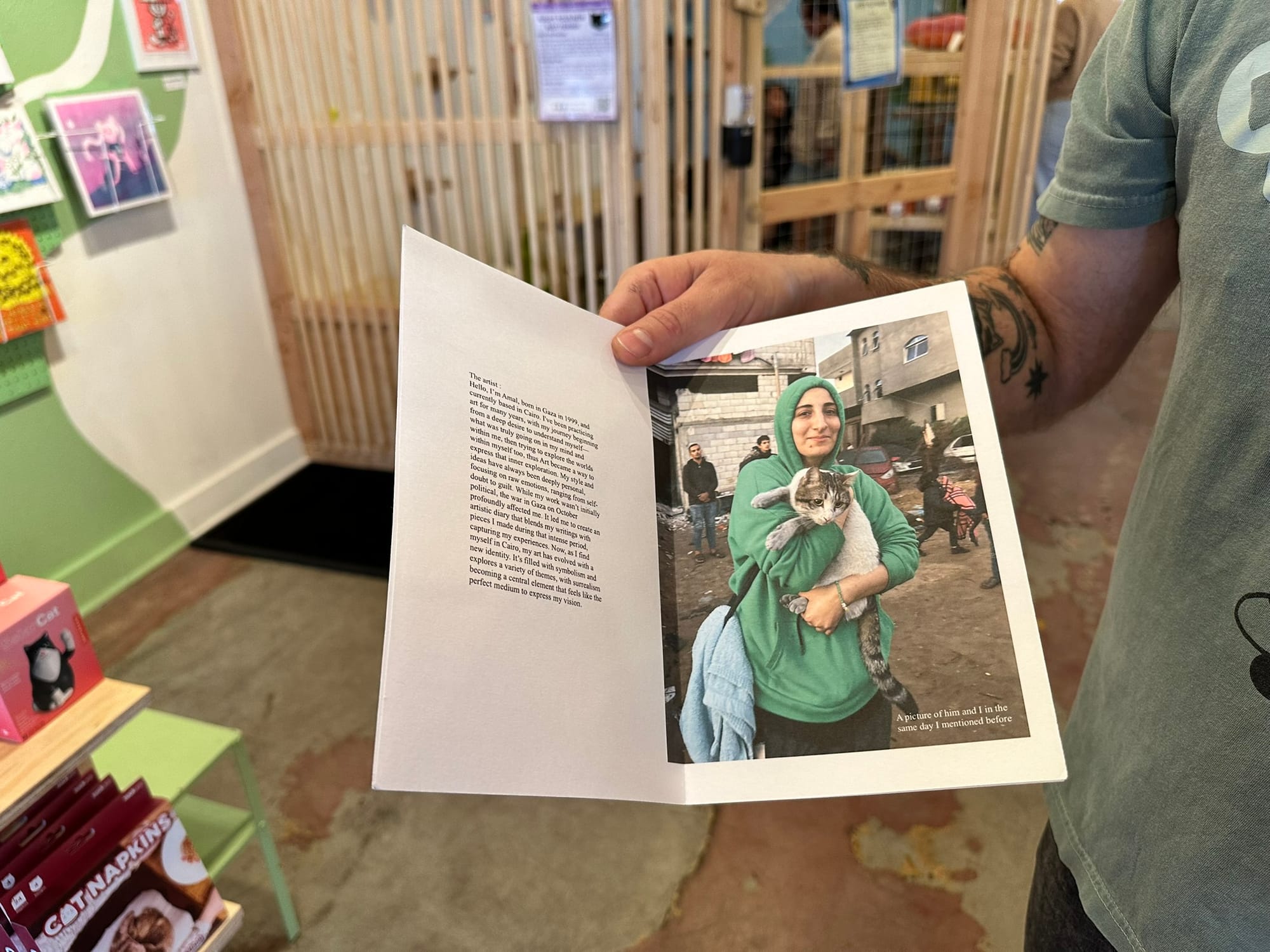 A person holding open a zine showing a woman cradling a white and gray cat.