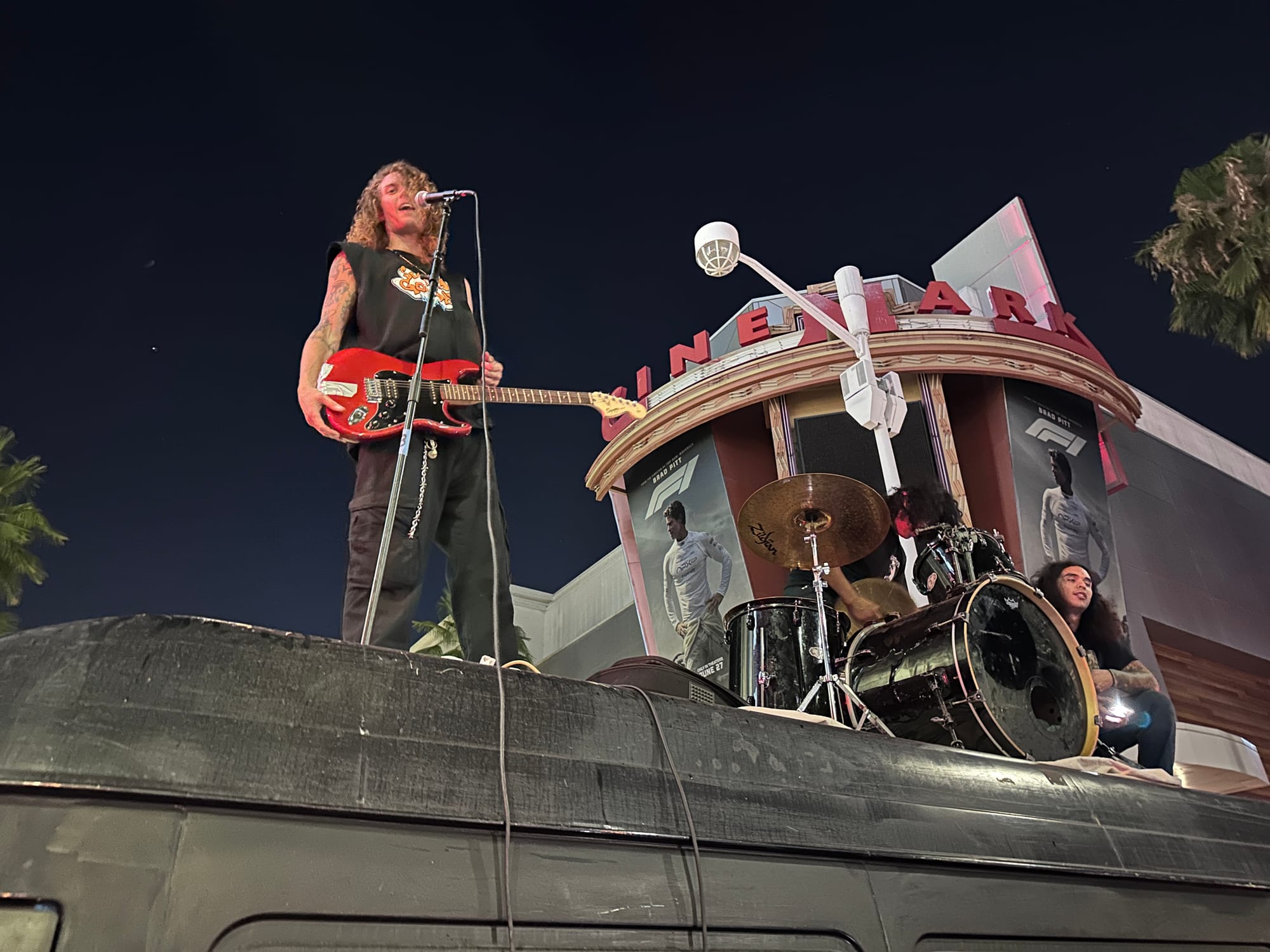 A guy stands on a van while holding a red guitar at night.