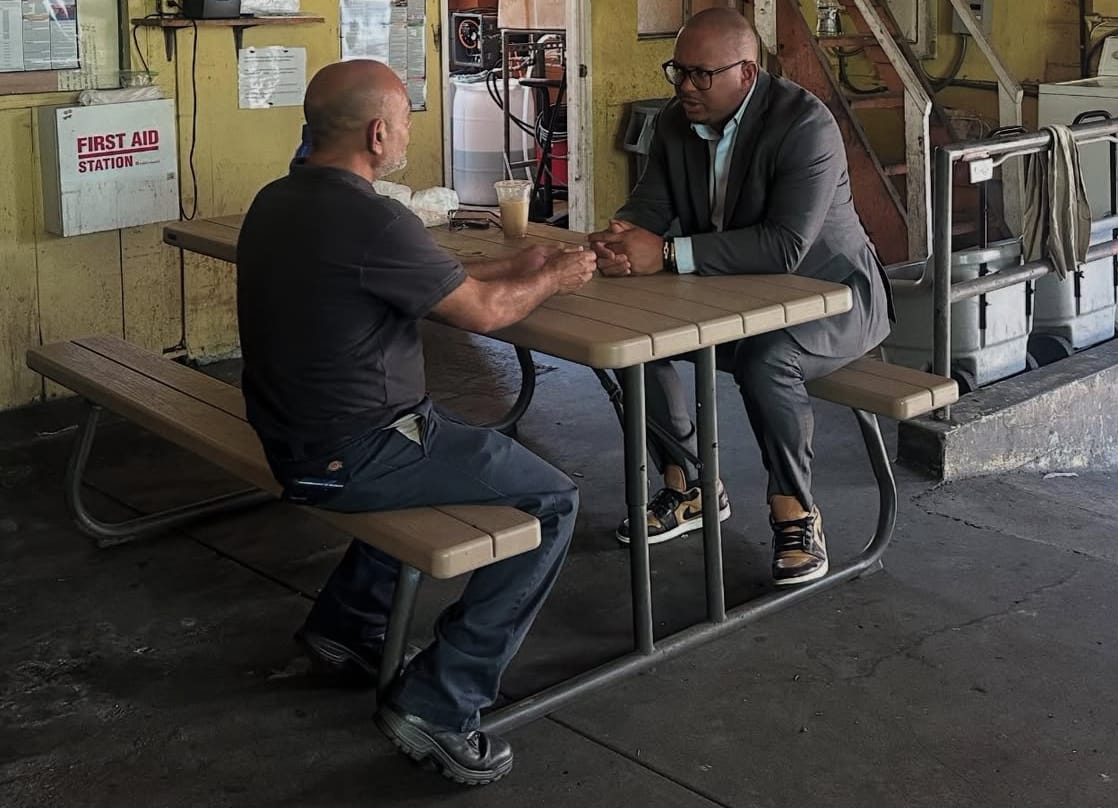 Two men sit across from each other at a table with bench seating.