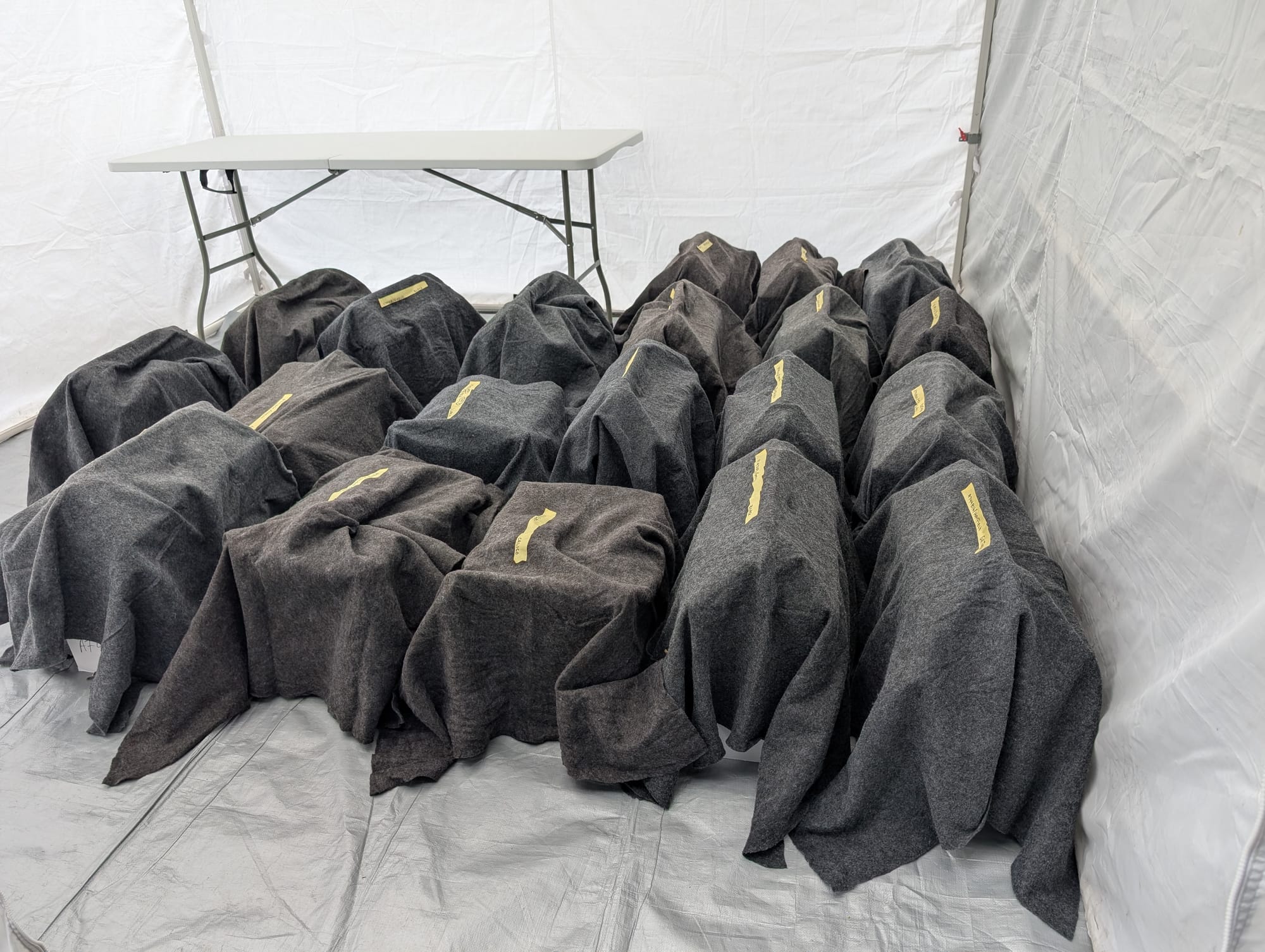 A large group of cat carriers all covered in gray blankets.