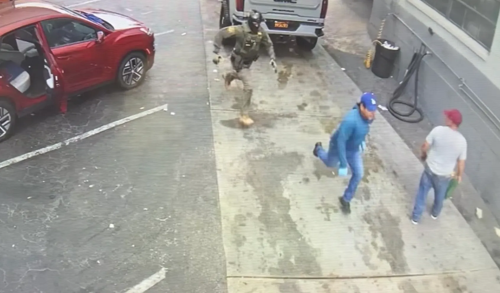 A man dressed in blue runs through a car wash while being chased by a man in a mask.