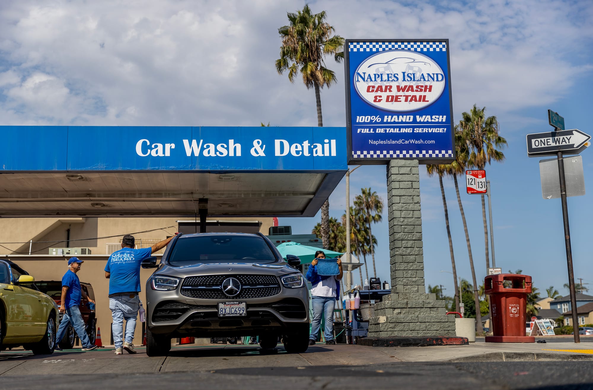 People stand next to a car near a sign saying "Naples Island Car Wash & Detail."