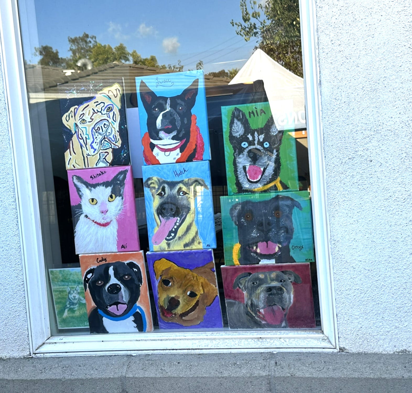 Nine paintings of dogs and cats cover a window.