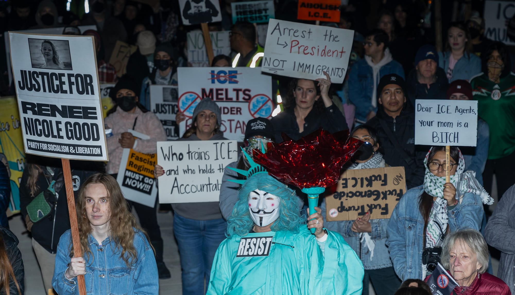 Dozens of people hold signs criticizing ICE at night.