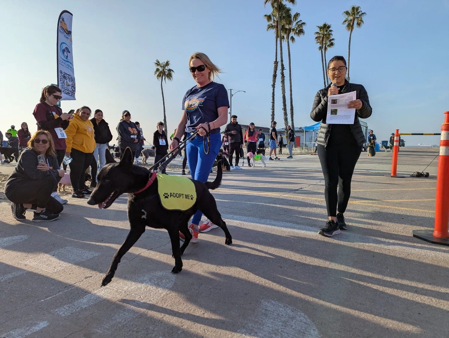 A woman holds onto a black dog with a leash as people look on.