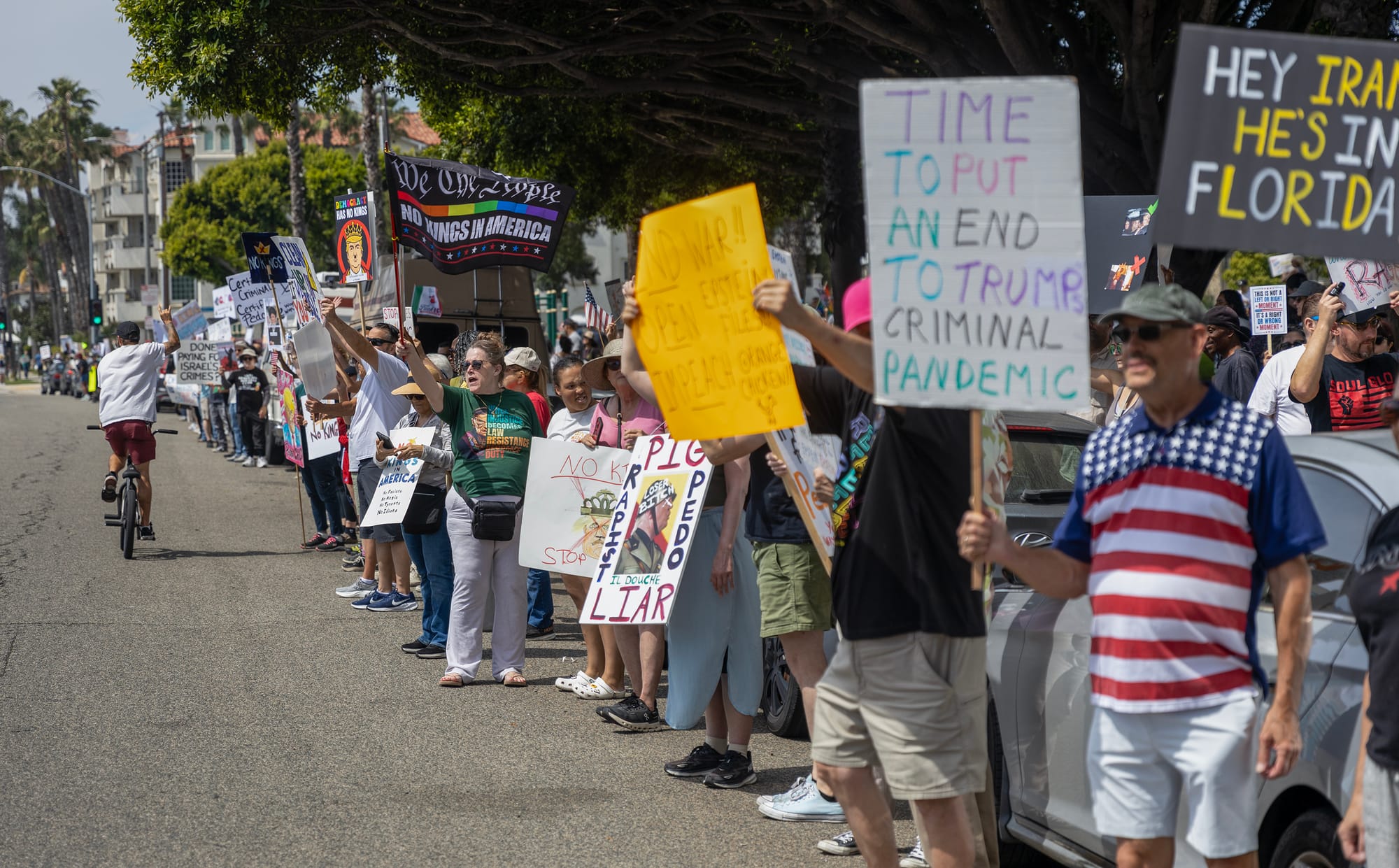 A long line of people stand along a street holding signs.