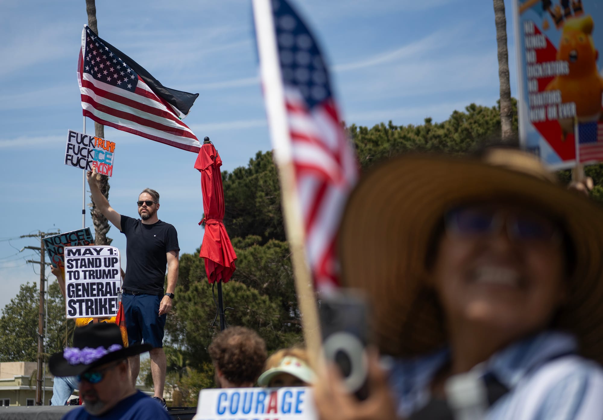 Two American flags fly above people holding signs.