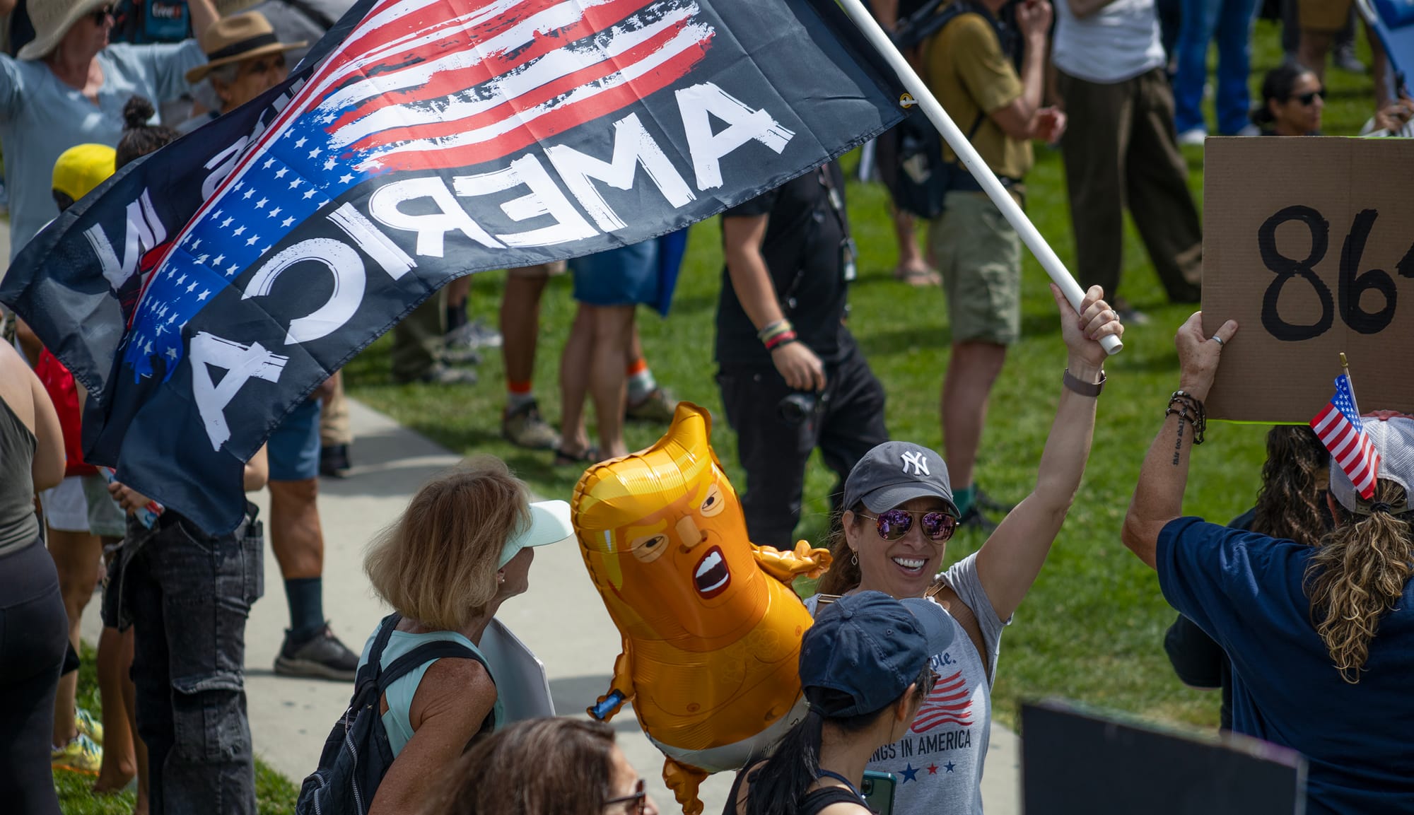 A smiling woman waves an upside-down American flag next to a cartoonish orange balloon of Donald Trump wearing a diaper.