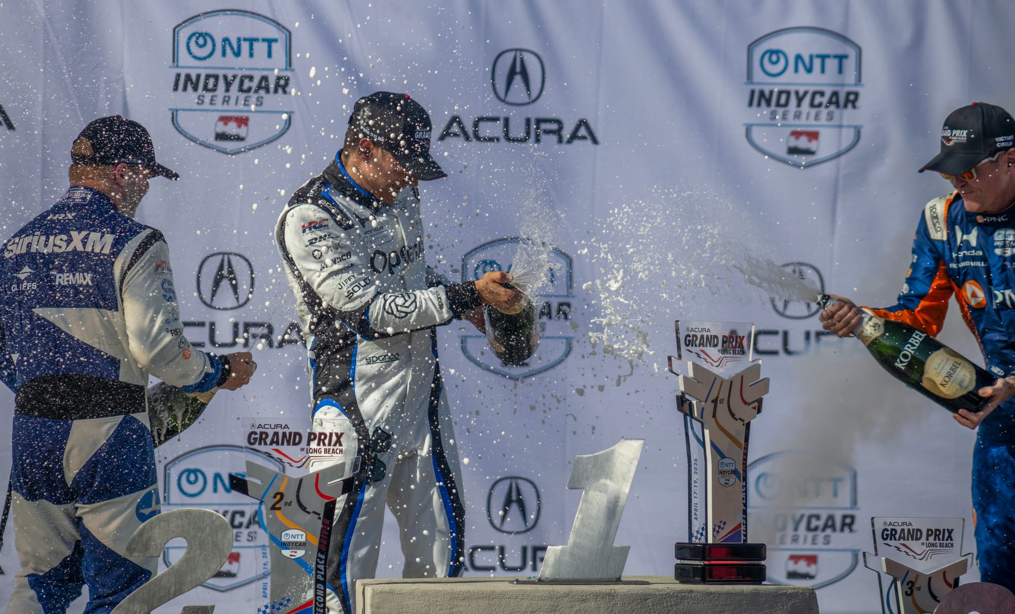 Three men spray freshly opened champagne into the air.