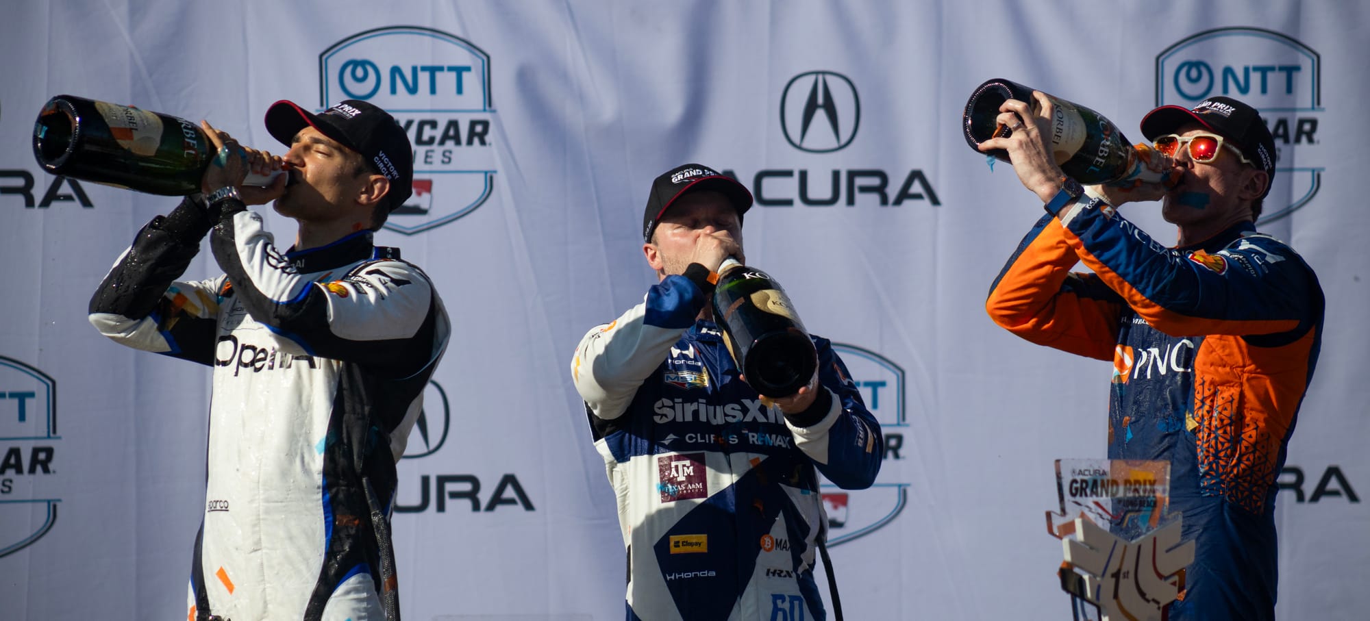 Three men drink from very large champagne bottles.